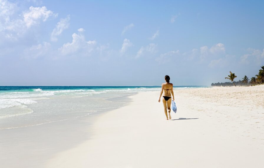 Woman walking down white sand beach Tulum