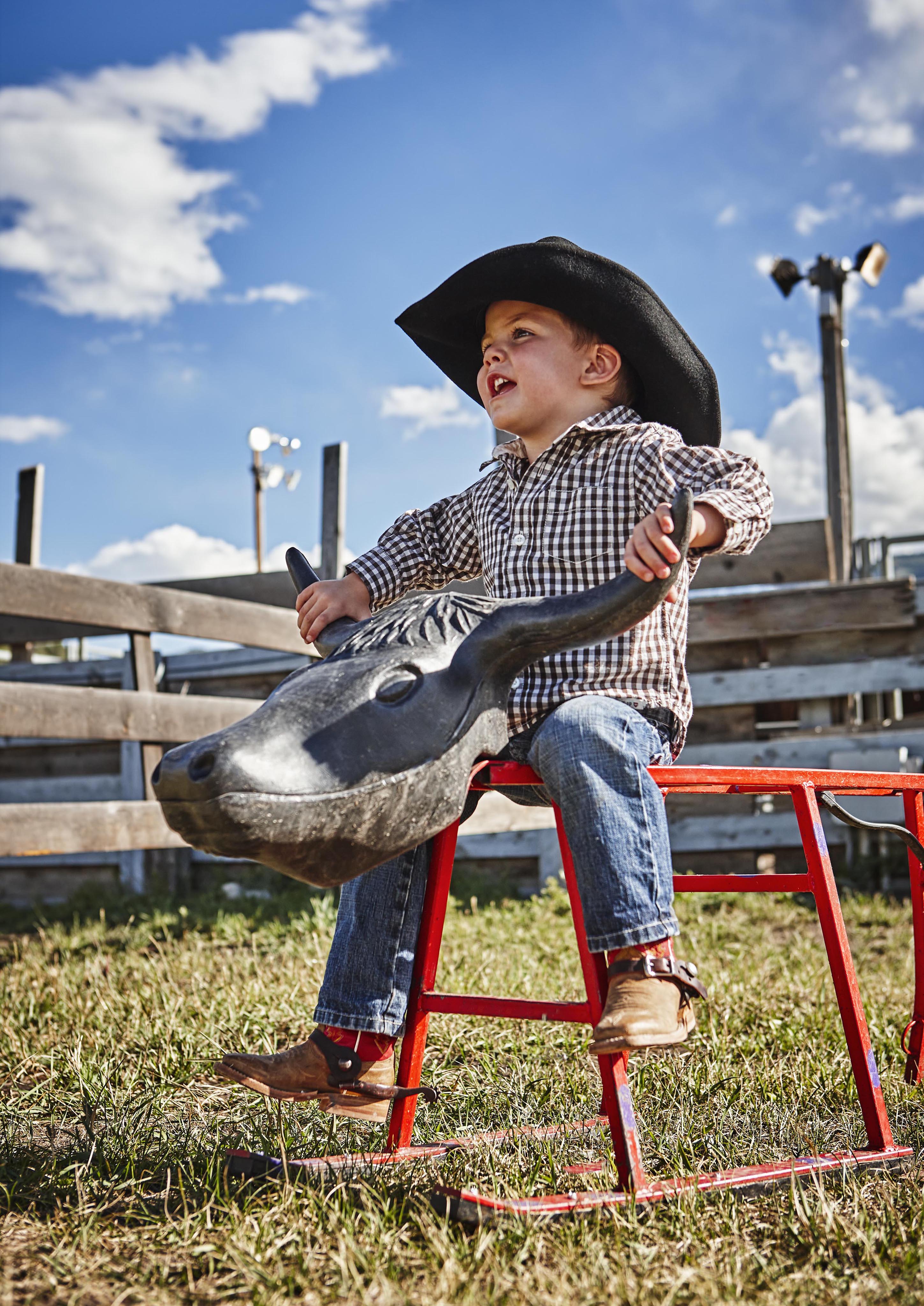 child wearing cowboy hat riding toy bull ride