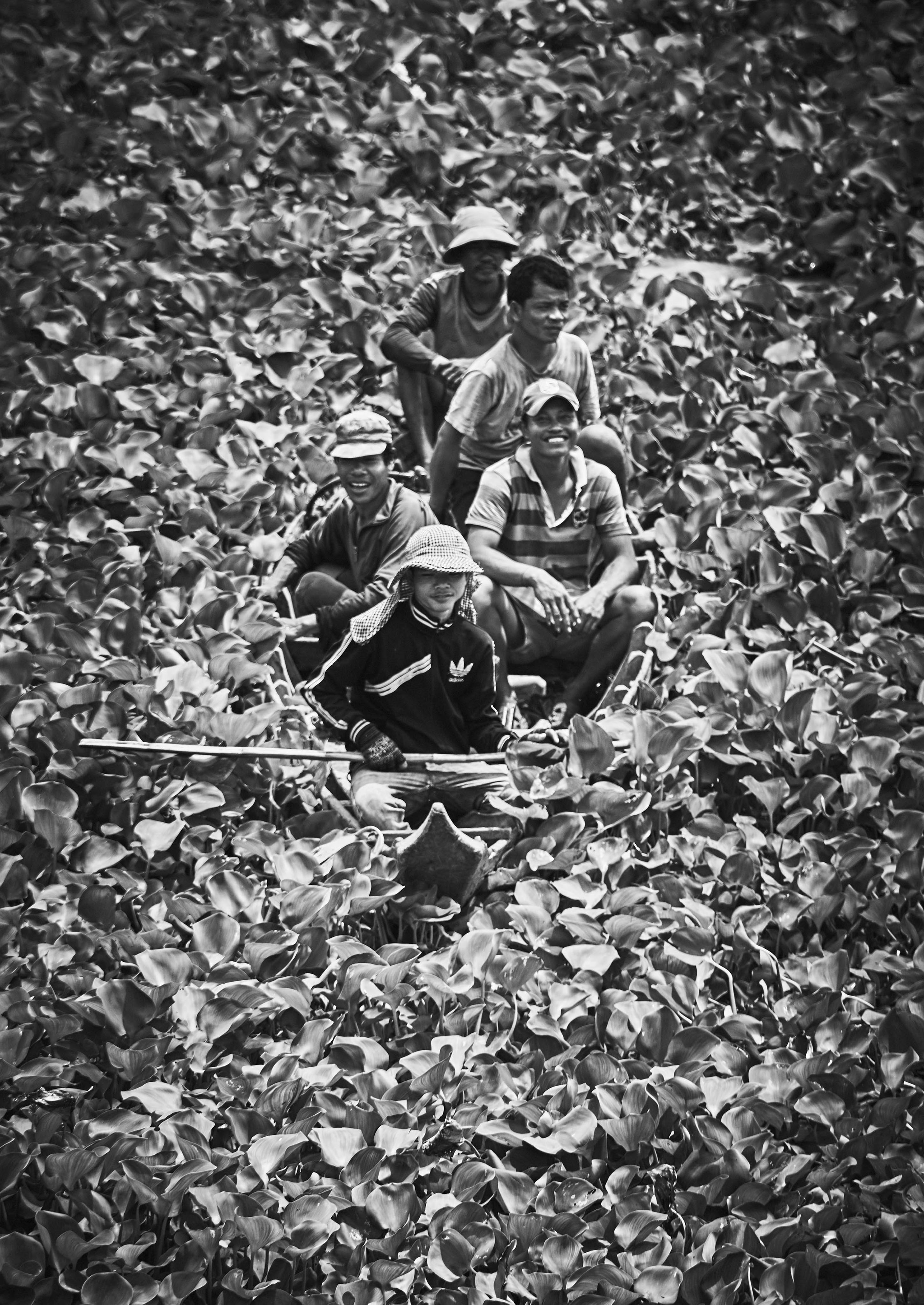 Four people in a small boat navigate through dense water plants, with one person in front holding a long stick.