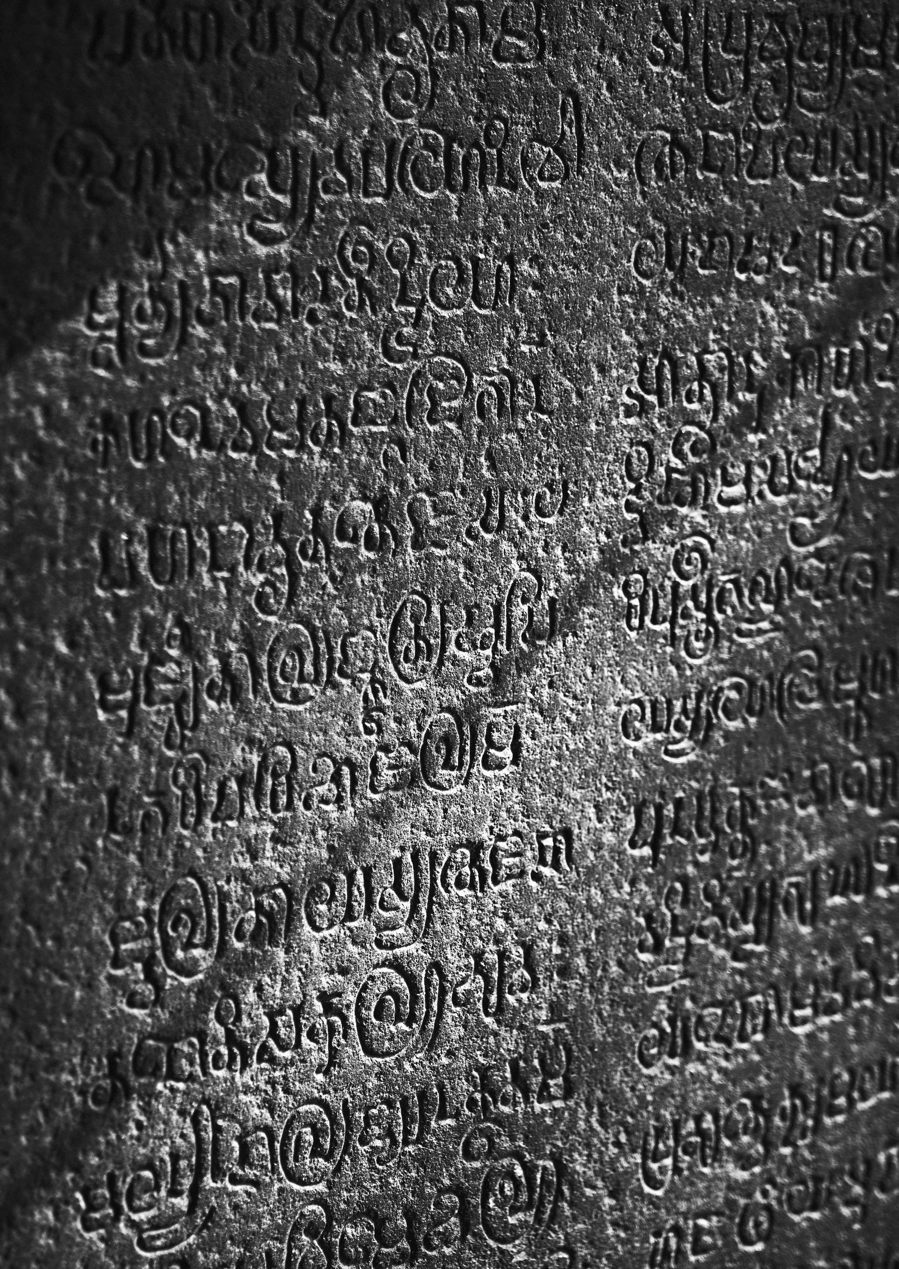 Close-up of ancient stone carving featuring intricate and detailed script with shadowed areas, highlighting the texture and craftsmanship.