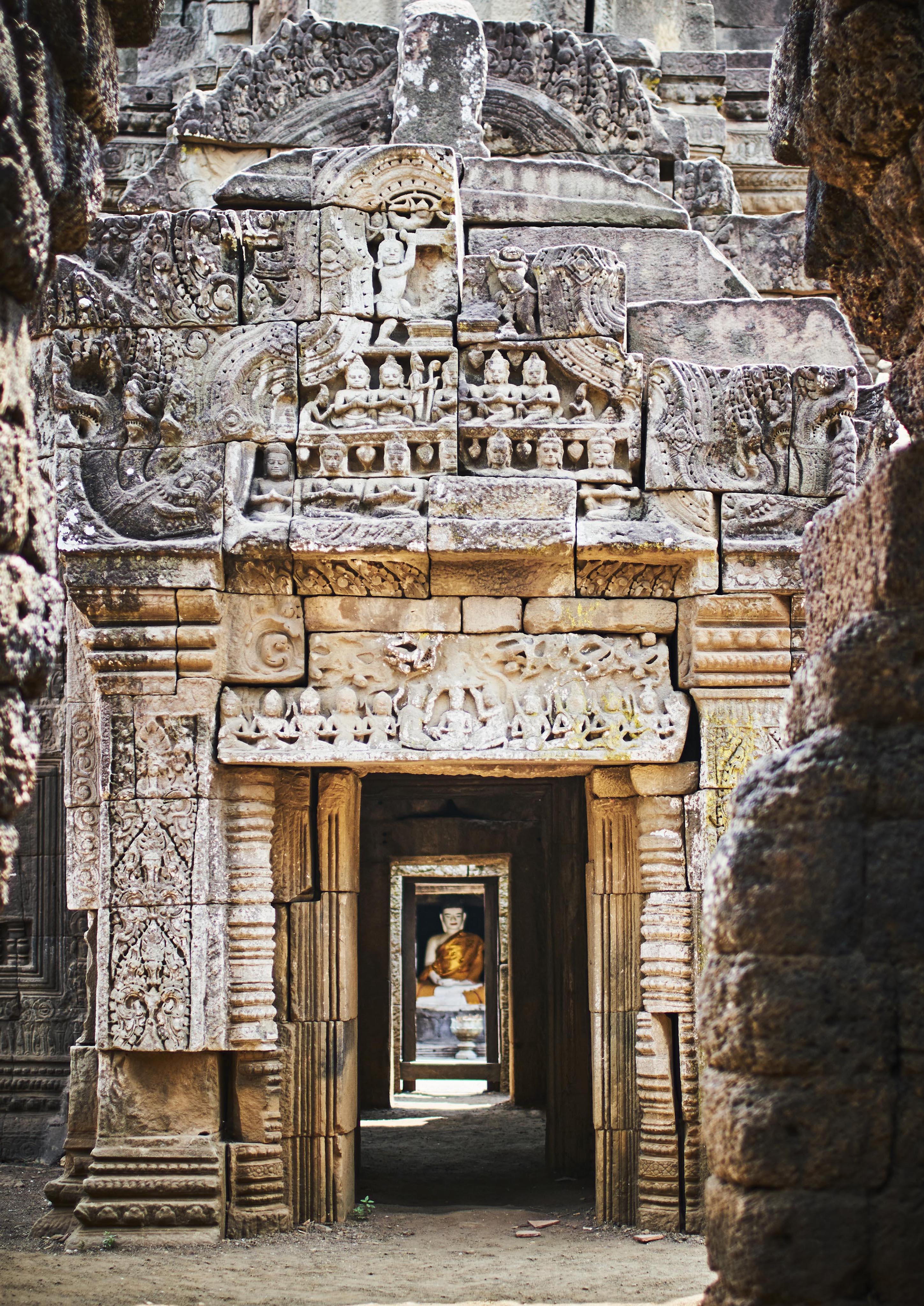 Stone temple corridor with intricately carved archways leading to a statue in the distance, featuring detailed bas-reliefs and erosion effects.