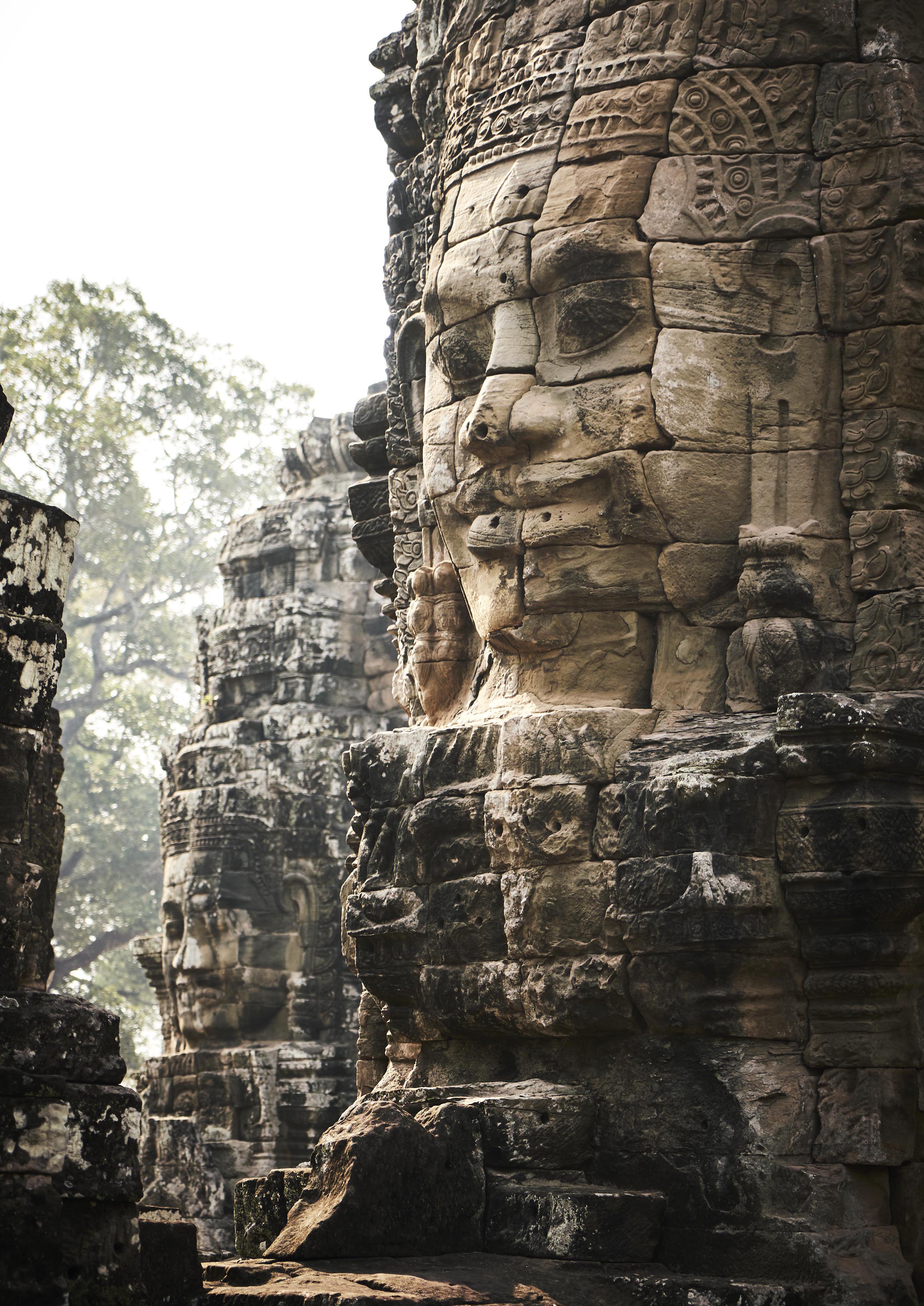 Close-up of ancient stone faces carved into the towers of Bayon Temple at Angkor, Cambodia, surrounded by trees.