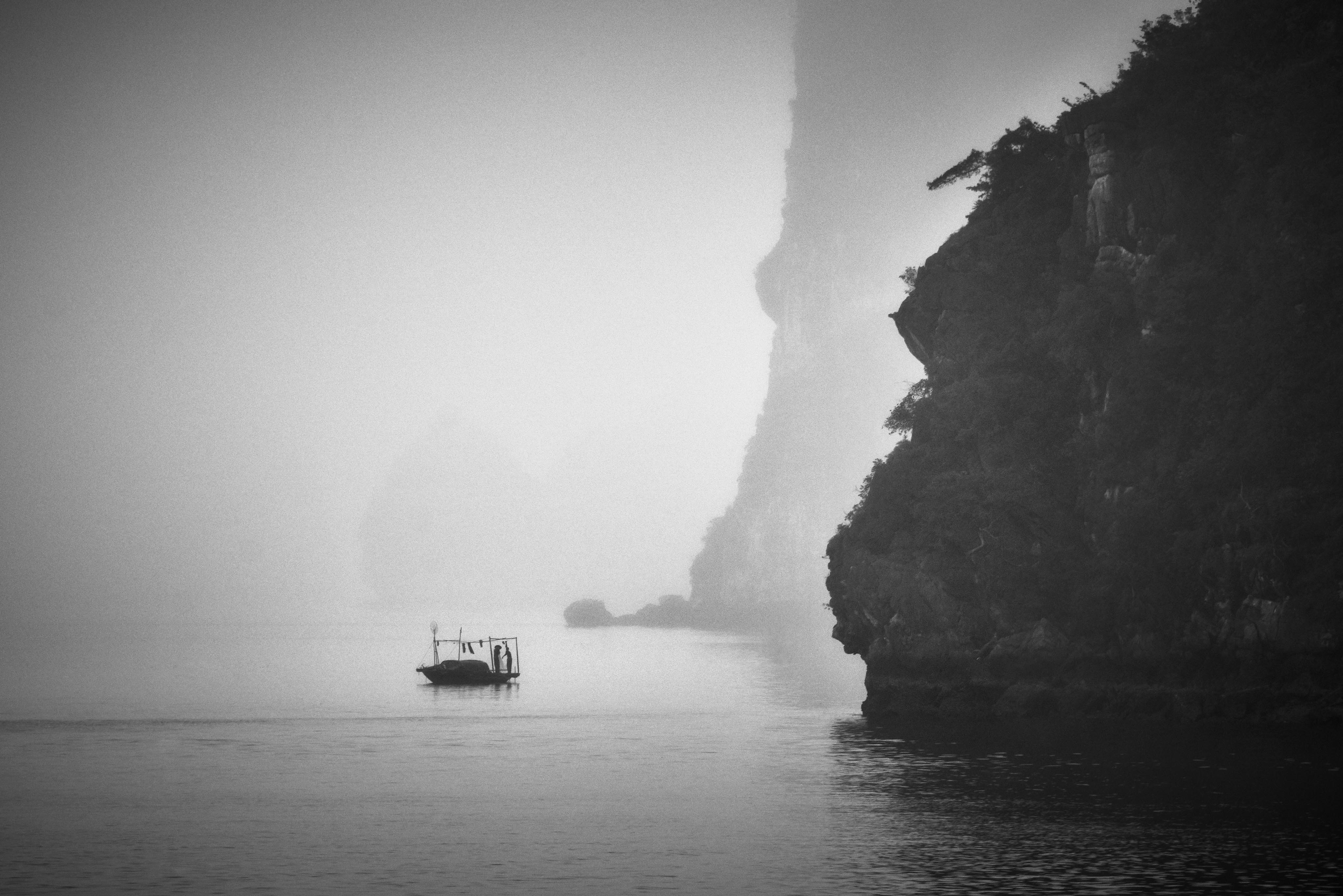 A small boat floats on calm water near misty rock formations, with fog obscuring the background.