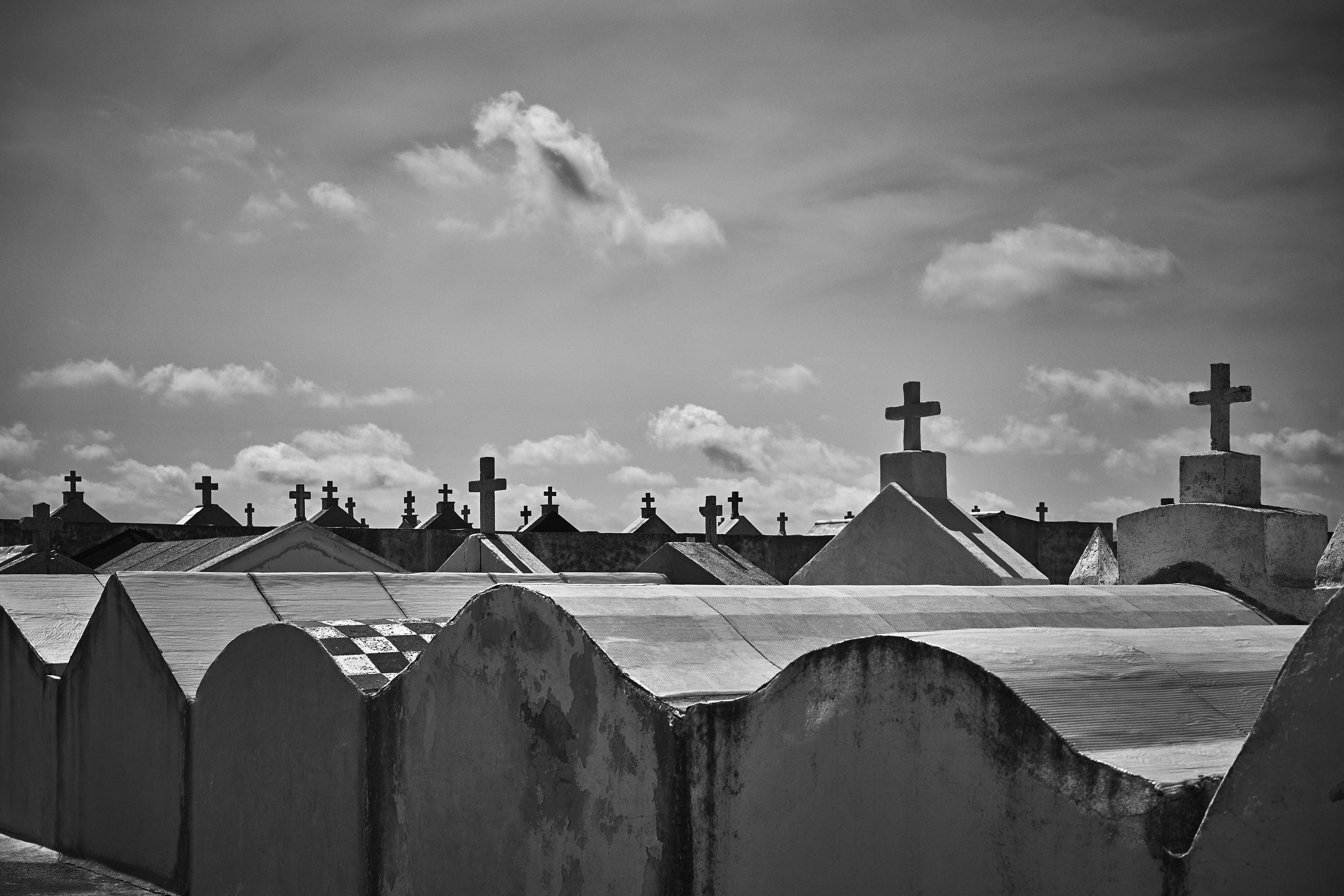 Black-and-white image of a cemetery with rows of above-ground tombs and crosses under a cloudy sky.