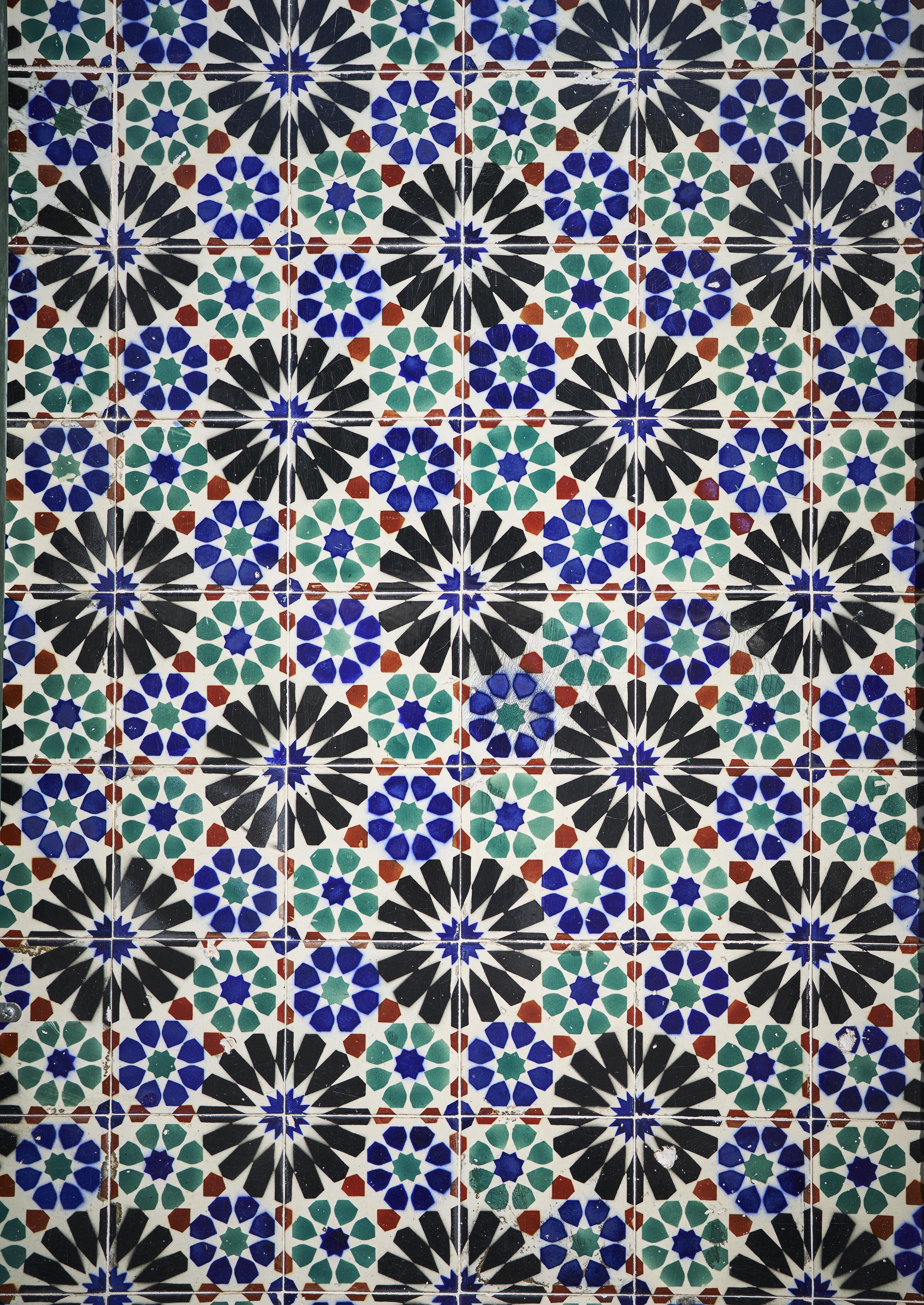 Colorful mosaic pattern featuring blue, green, black, and red geometric shapes, arranged in a repetitive, symmetrical design.