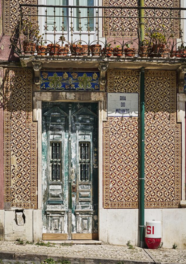Ornate tiled building facade with a weathered wooden double door, a street sign reading "Rua do Mirante," and a red and white fire hydrant marked "SI" on a cobblestone sidewalk.