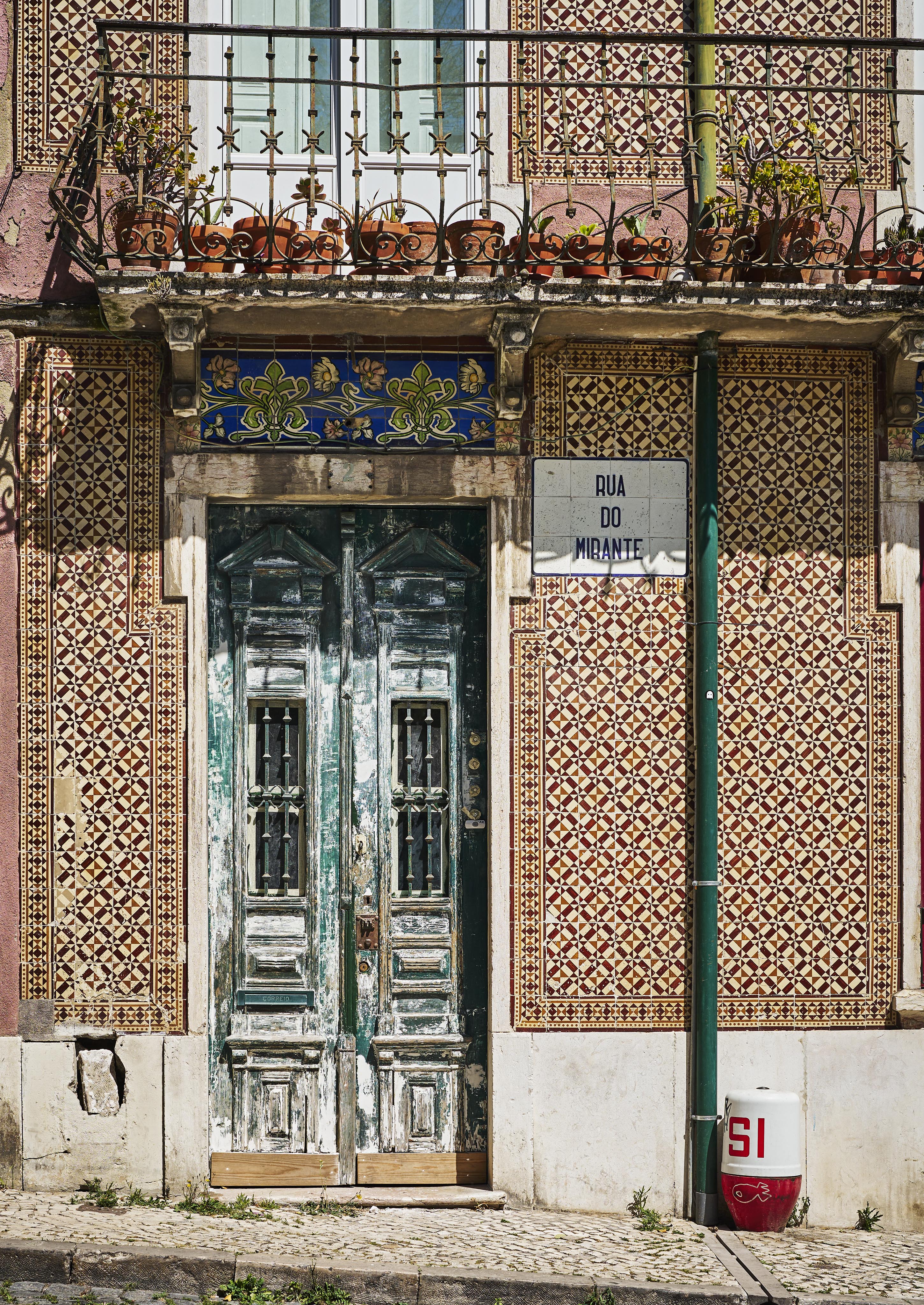 Ornate tiled building facade with a weathered wooden double door, a street sign reading "Rua do Mirante," and a red and white fire hydrant marked "SI" on a cobblestone sidewalk.