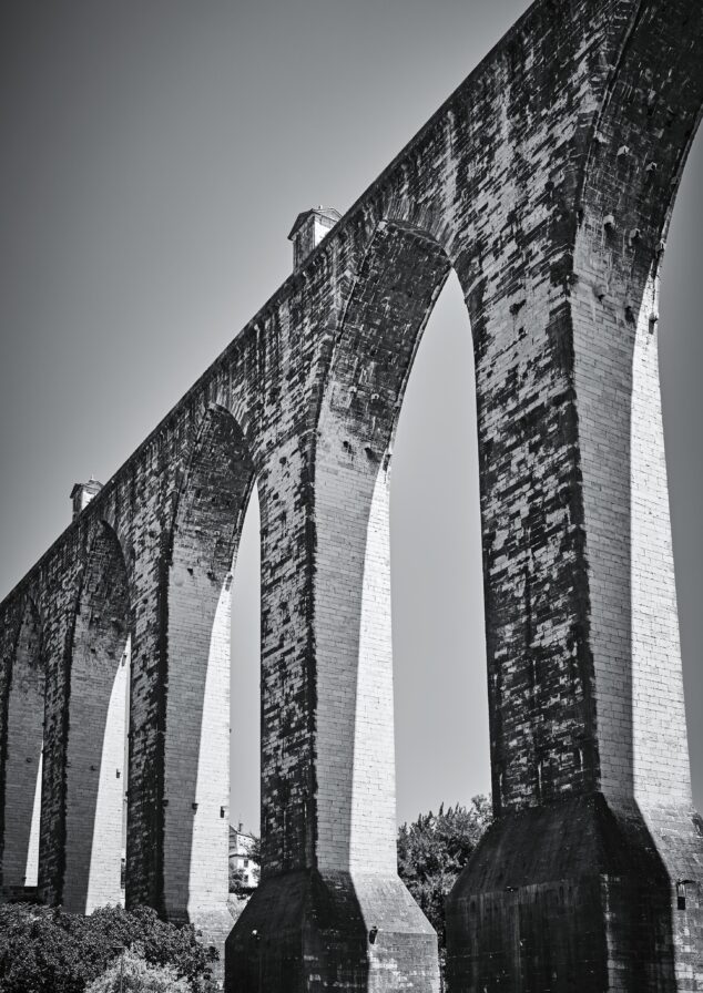 Black and white photo of a large stone aqueduct with multiple arches, against a clear sky.