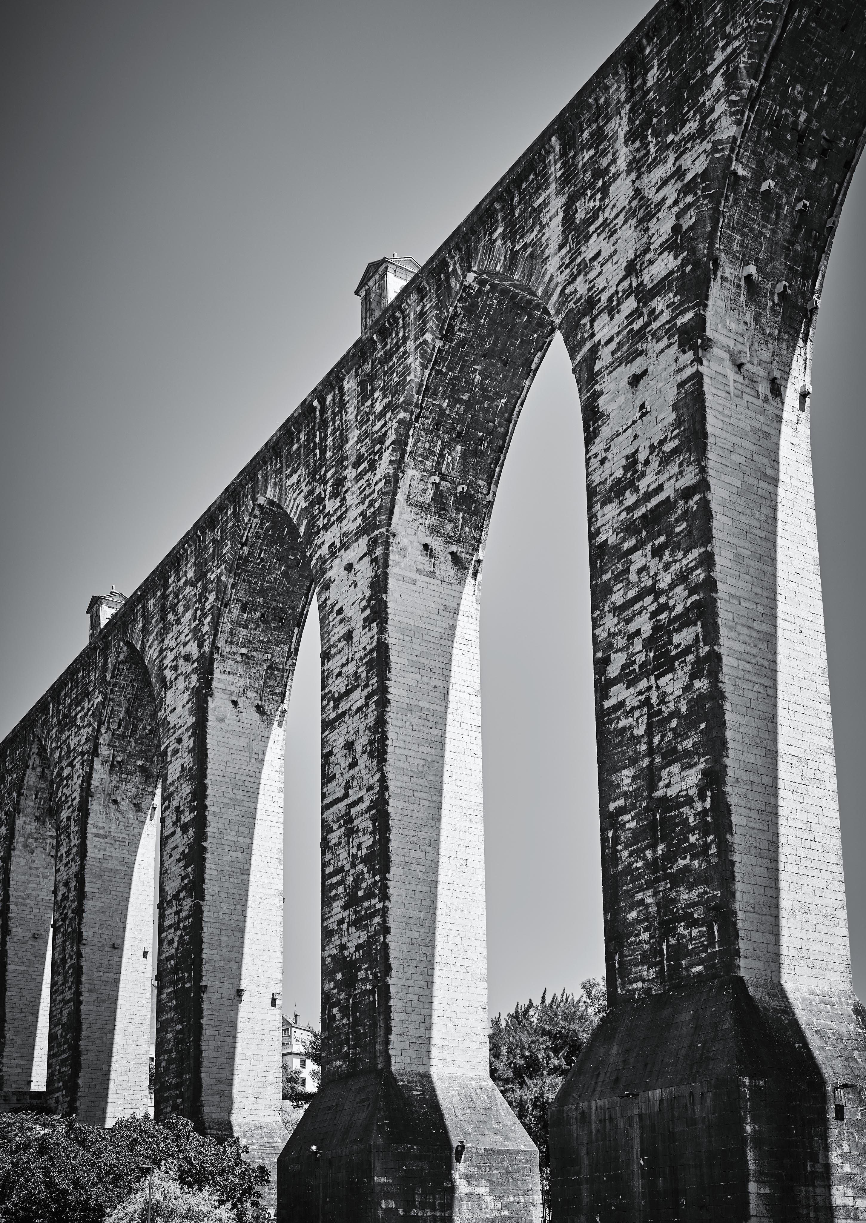 Black and white photo of a large stone aqueduct with multiple arches, against a clear sky.