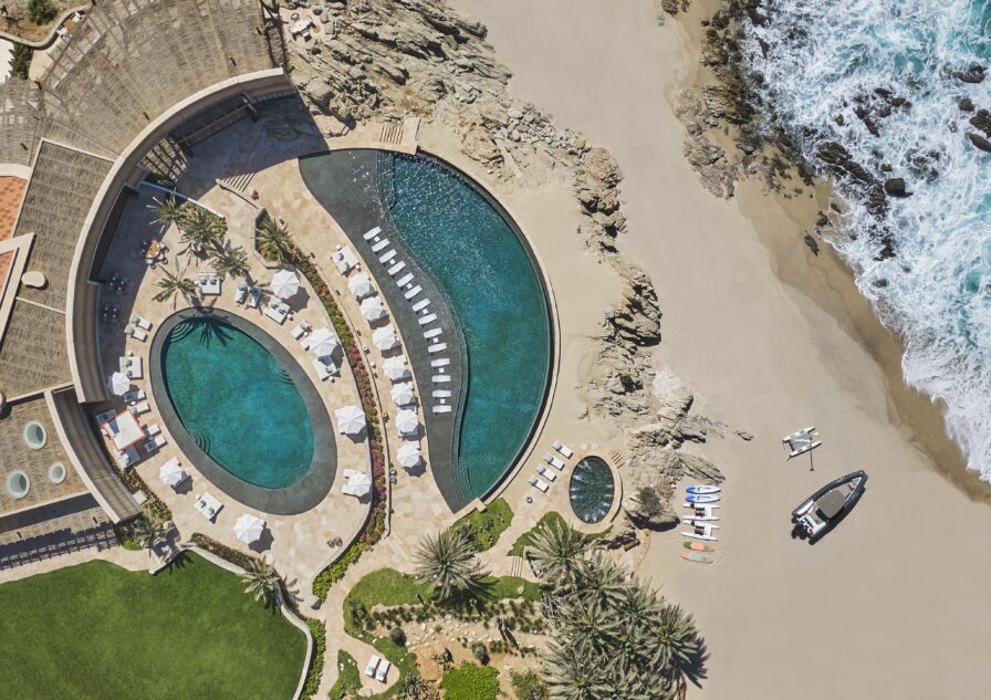Aerial of large round pools at luxury Baja Cove Club at Cabo Del Sol with palm trees and surf
