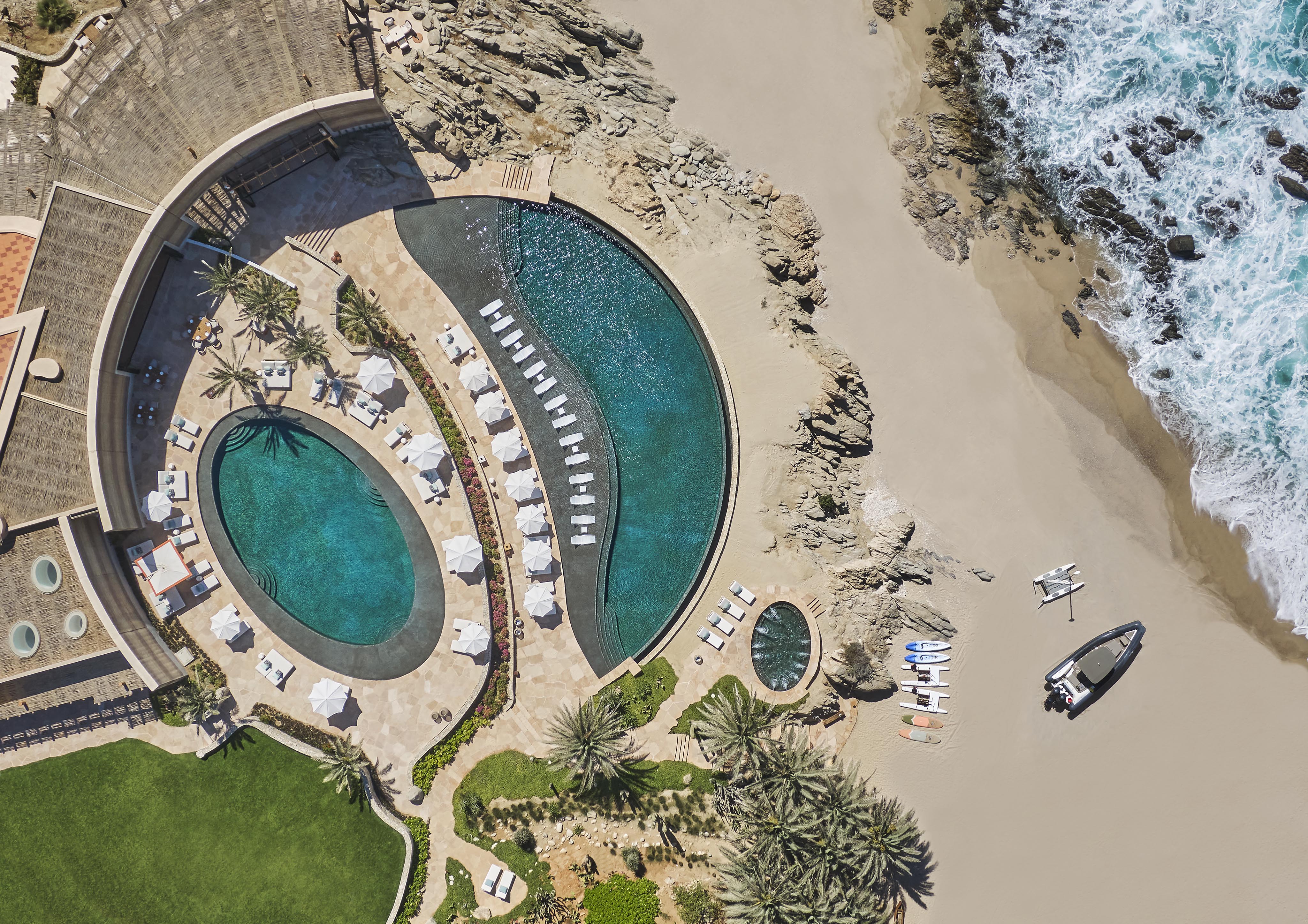 Aerial of large round pools at luxury Baja Cove Club at Cabo Del Sol with palm trees and surf