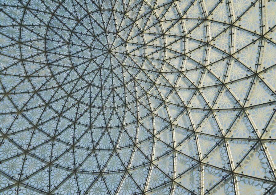 A detail view of landmark structure Abu Dhabi Grand Mosque with glass dome ceiling with a geometric metal framework and patterned panels forming a symmetrical, intricate design.