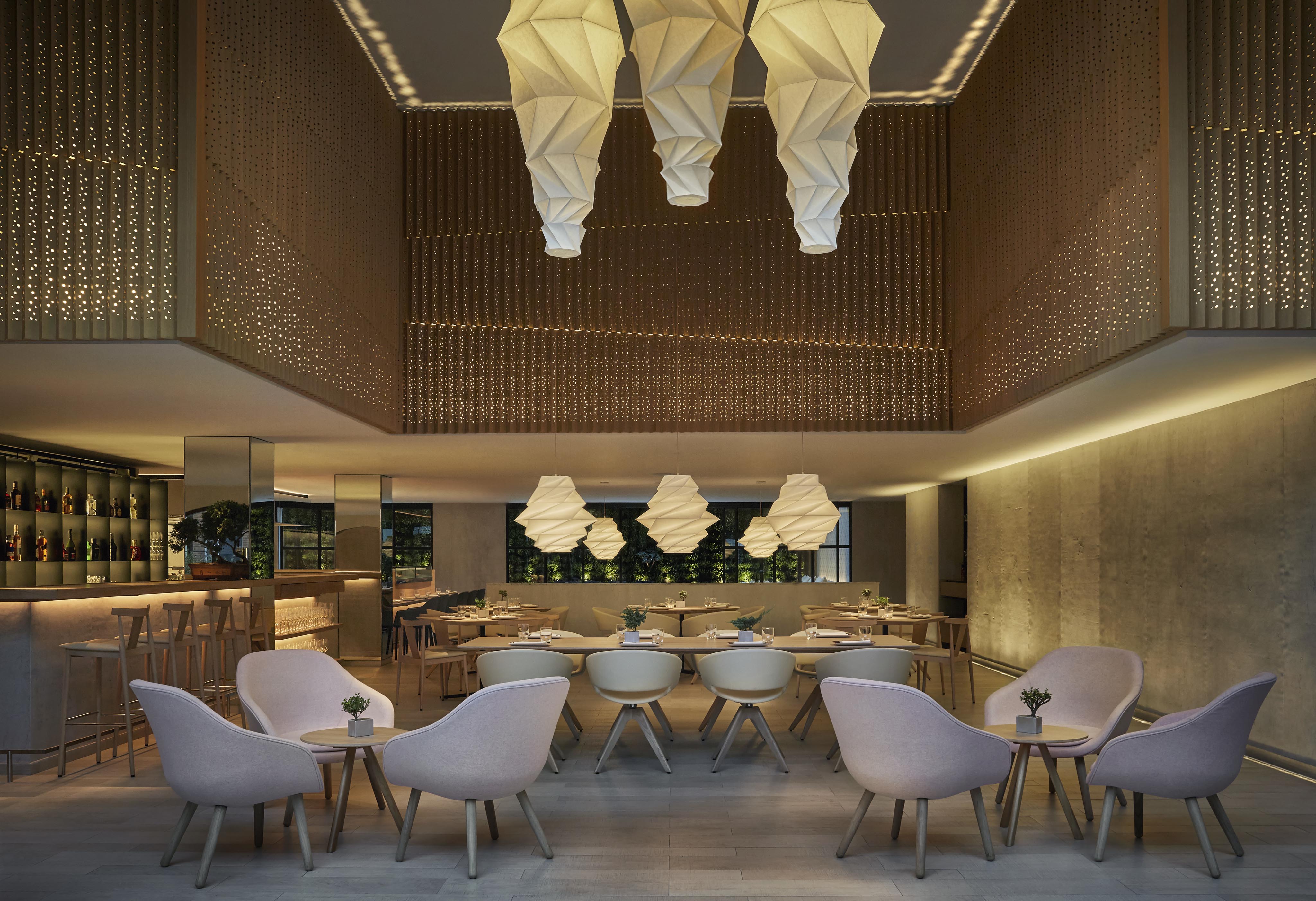 Modern restaurant interior with geometric lighting fixtures, beige chairs, and round tables. A bar inspired by Central America is visible on the left, along with shelves of bottles.