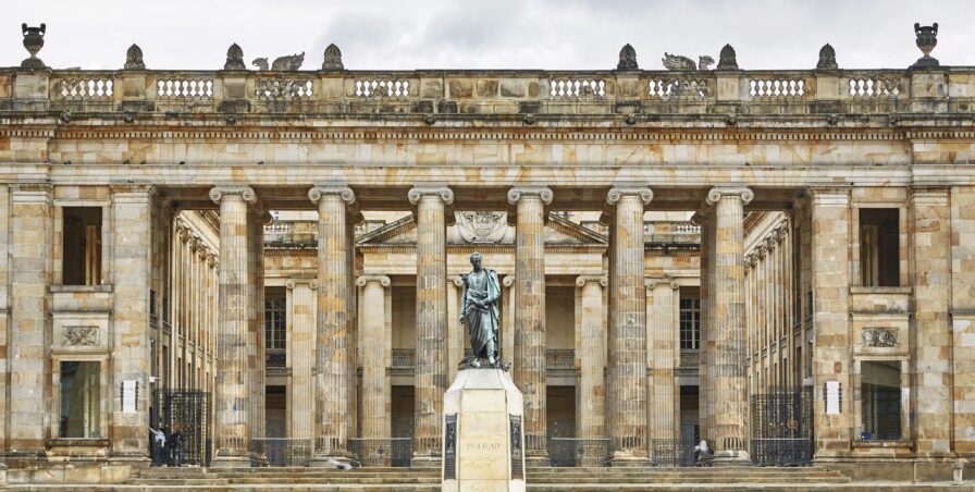 Stone building with tall columns and a statue in front, under a cloudy sky, reminiscent of historic South America. Plaque reads "Nariño.”.