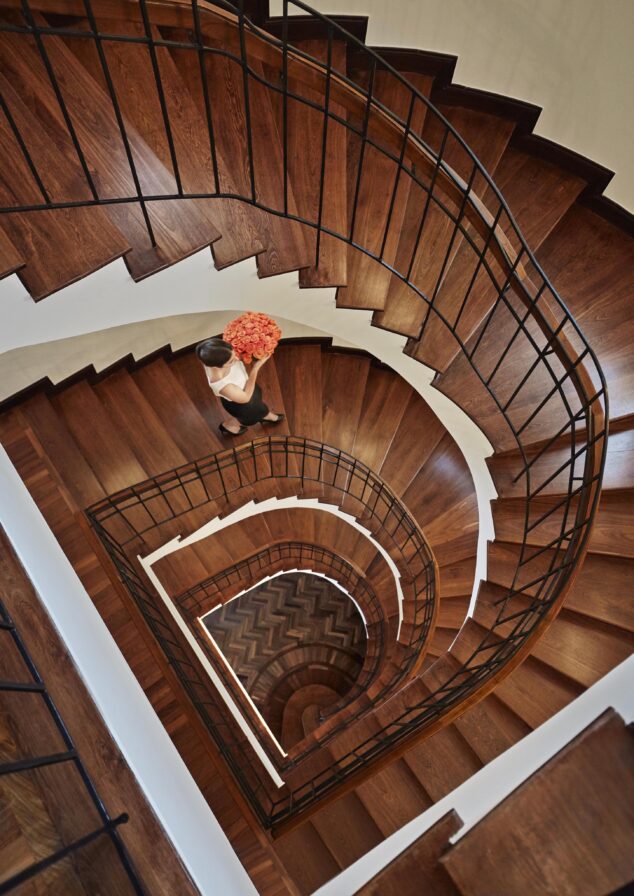 Four Seasons Bogota hospitality staff carrying a bouquet of orange flowers descending a spiral wooden staircase with black railings.