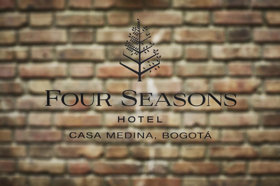 A sign on a brick wall reads "Four Seasons Hotel Casa Medina, Bogotá," with a decorative tree logo above the text, elegantly capturing the charm of South America.