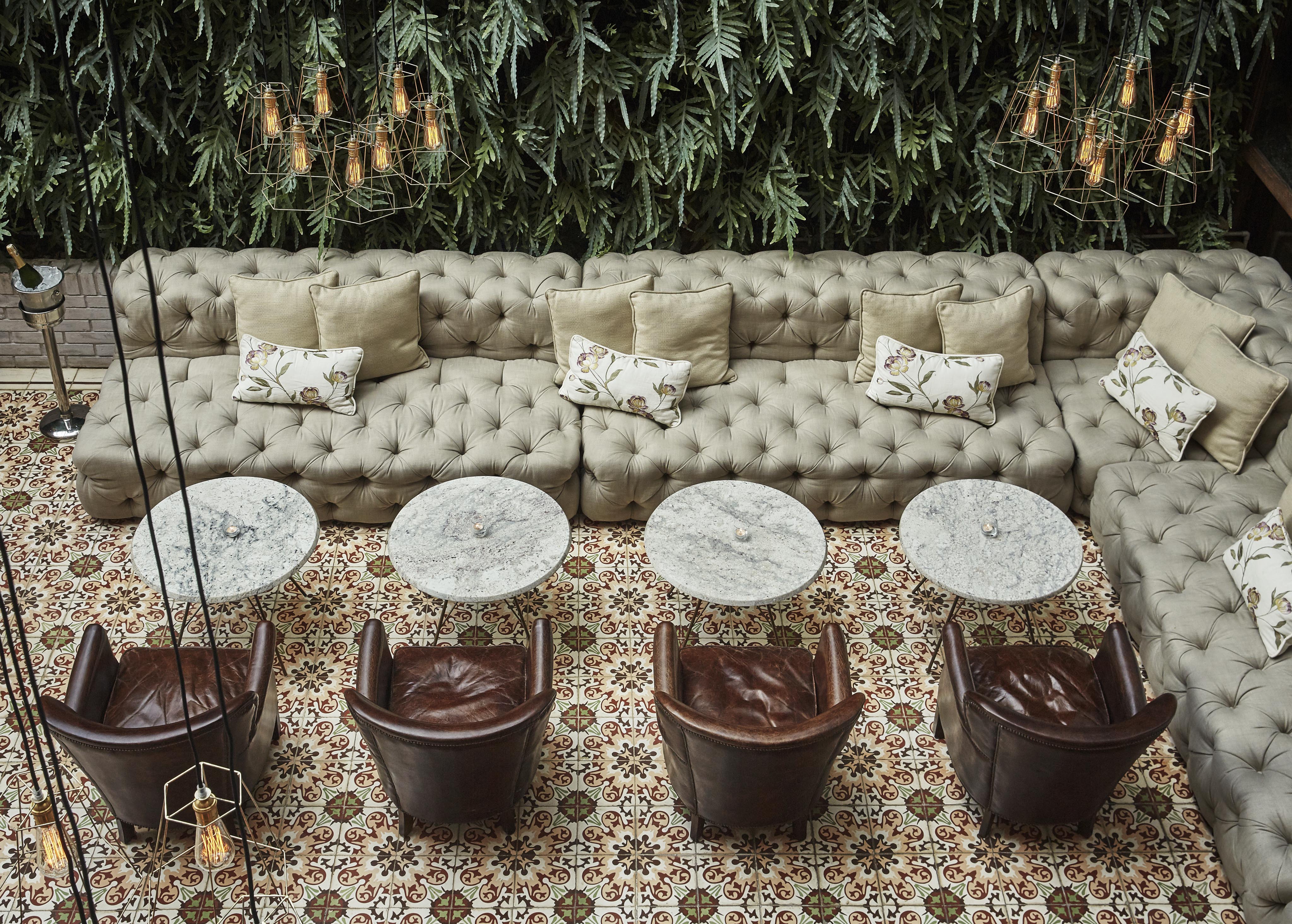 Aerial view of a Four Seasons Casa Medina Bogota lounge area with a long tufted sofa, floral cushions, round marble tables, and leather chairs, set against a wall with lush greenery reminiscent of lush Central American jungles.