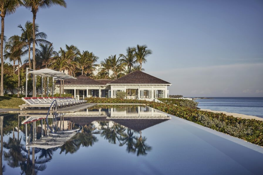The Ocean Club, A Four Seasons Resort, renowned for its luxurious beachfront location with a reflective infinity pool, surrounded by palm trees, and a clear blue sky.