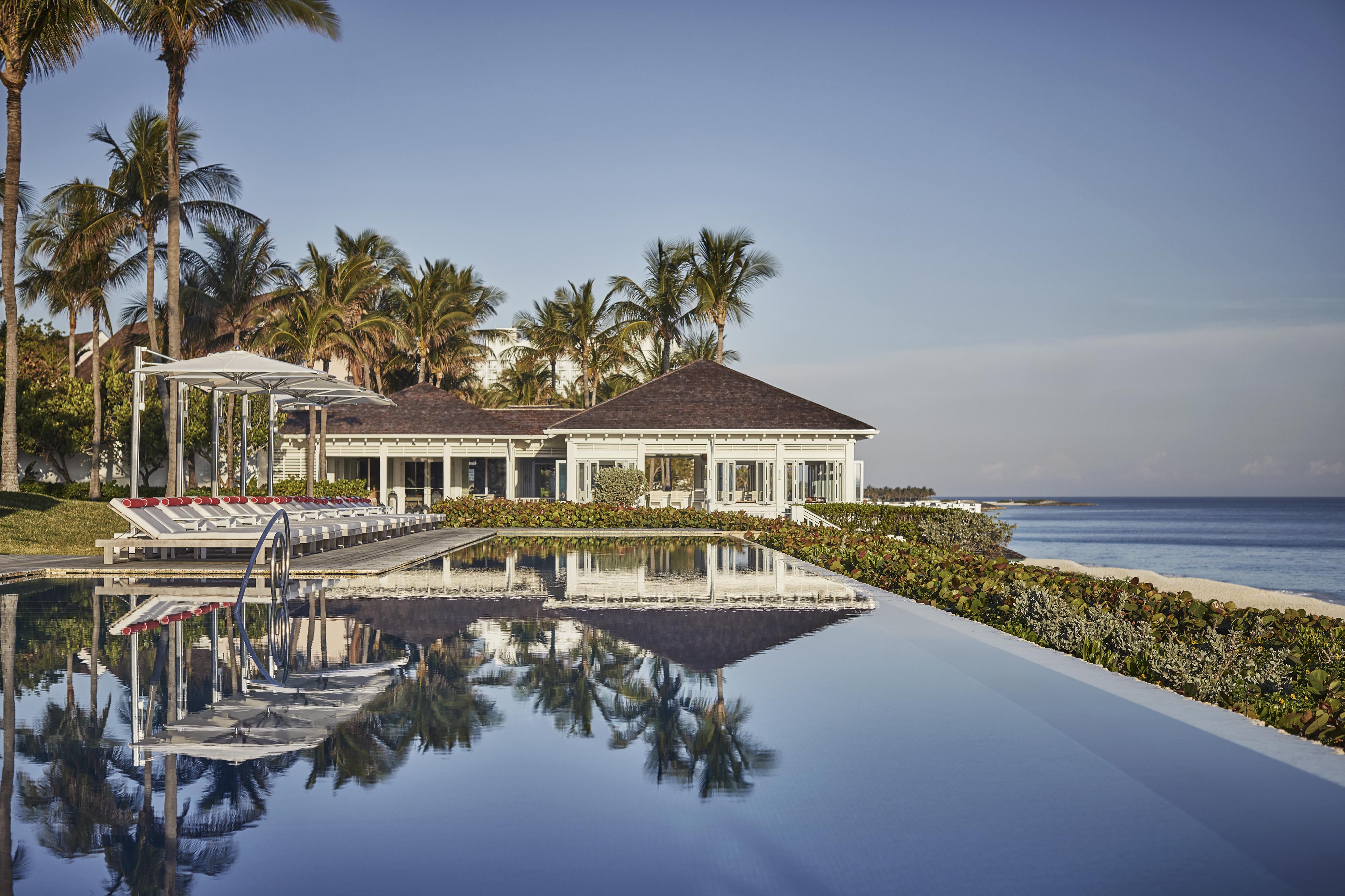 The Ocean Club, A Four Seasons Resort, renowned for its luxurious beachfront location with a reflective infinity pool, surrounded by palm trees, and a clear blue sky.