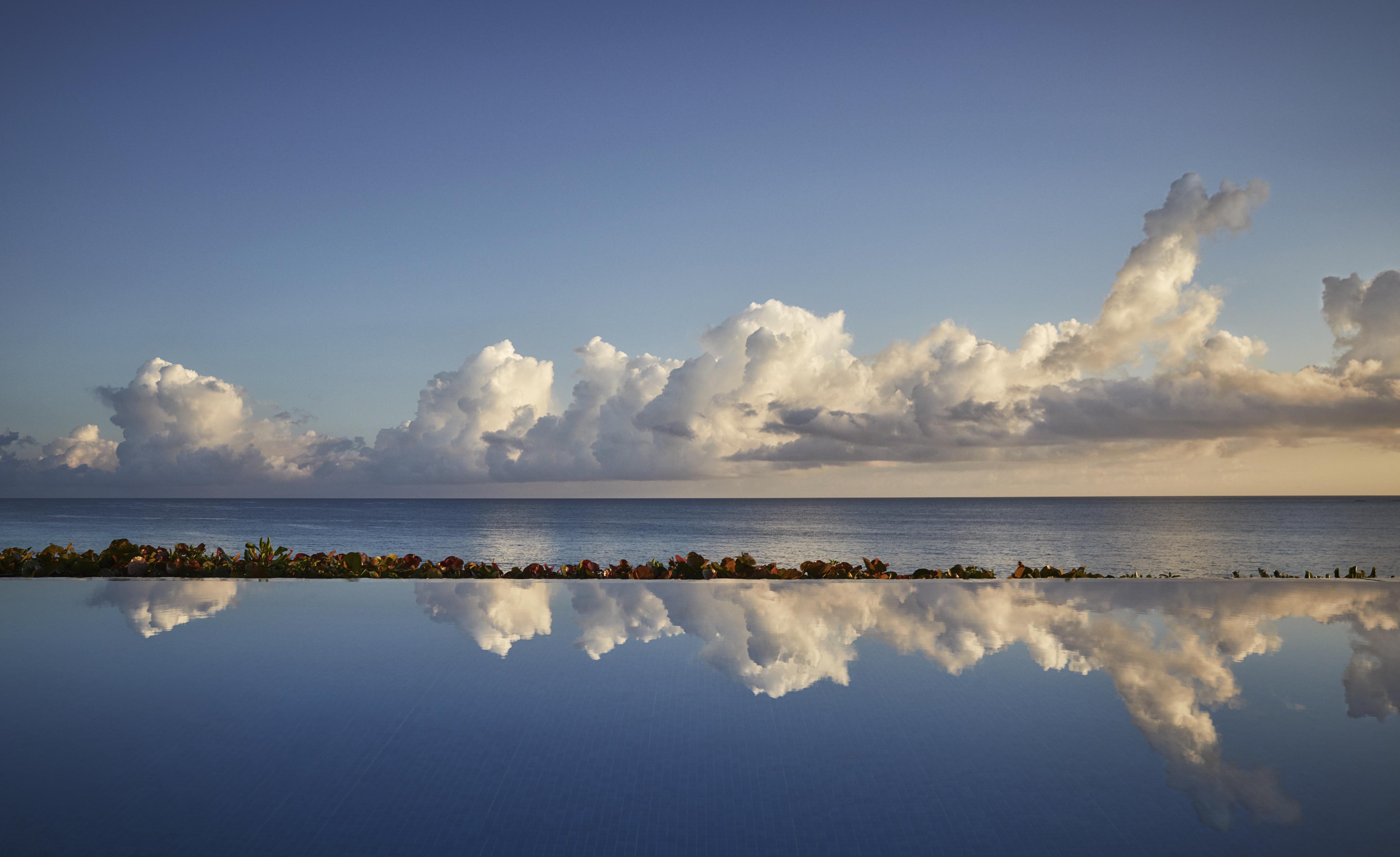 Four Seasons Ocean Club infinity pool reflecting clouds under a clear sky with ocean in the background.