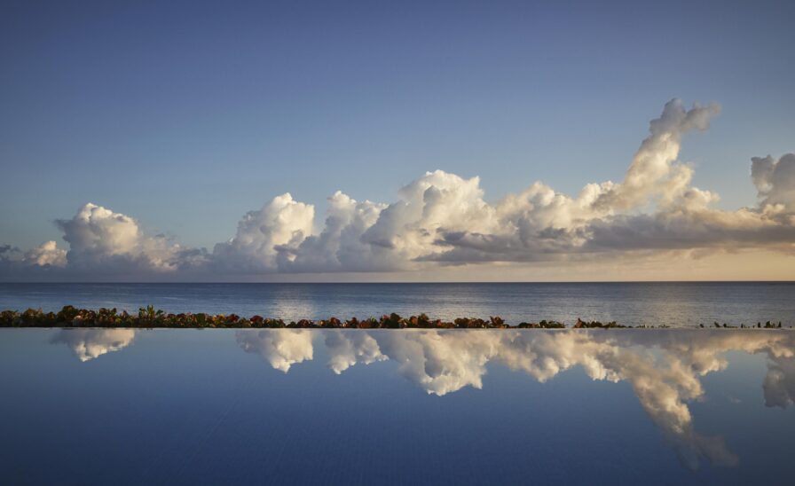 The Ocean Club, A Four Seasons Resort pristine infinity pool reflecting clouds with Bahamas ocean and sky in the background.