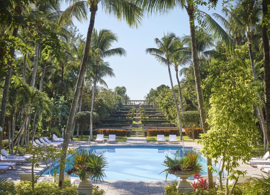 Outdoor Four Seasons Ocean Club resort swimming pool surrounded by palm trees and luxury lounge chairs, with landmark Paradise Island Versailles gardens and lush greenery extending into the distance.