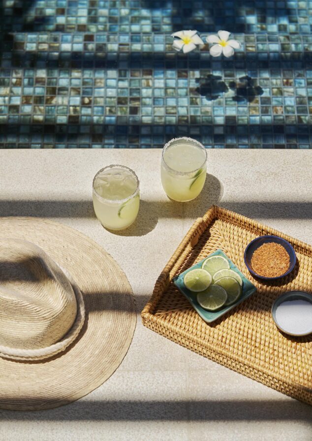 Top down view of resort cadillac margaritas served poolside with salt, lime, and spices on woven tray.
