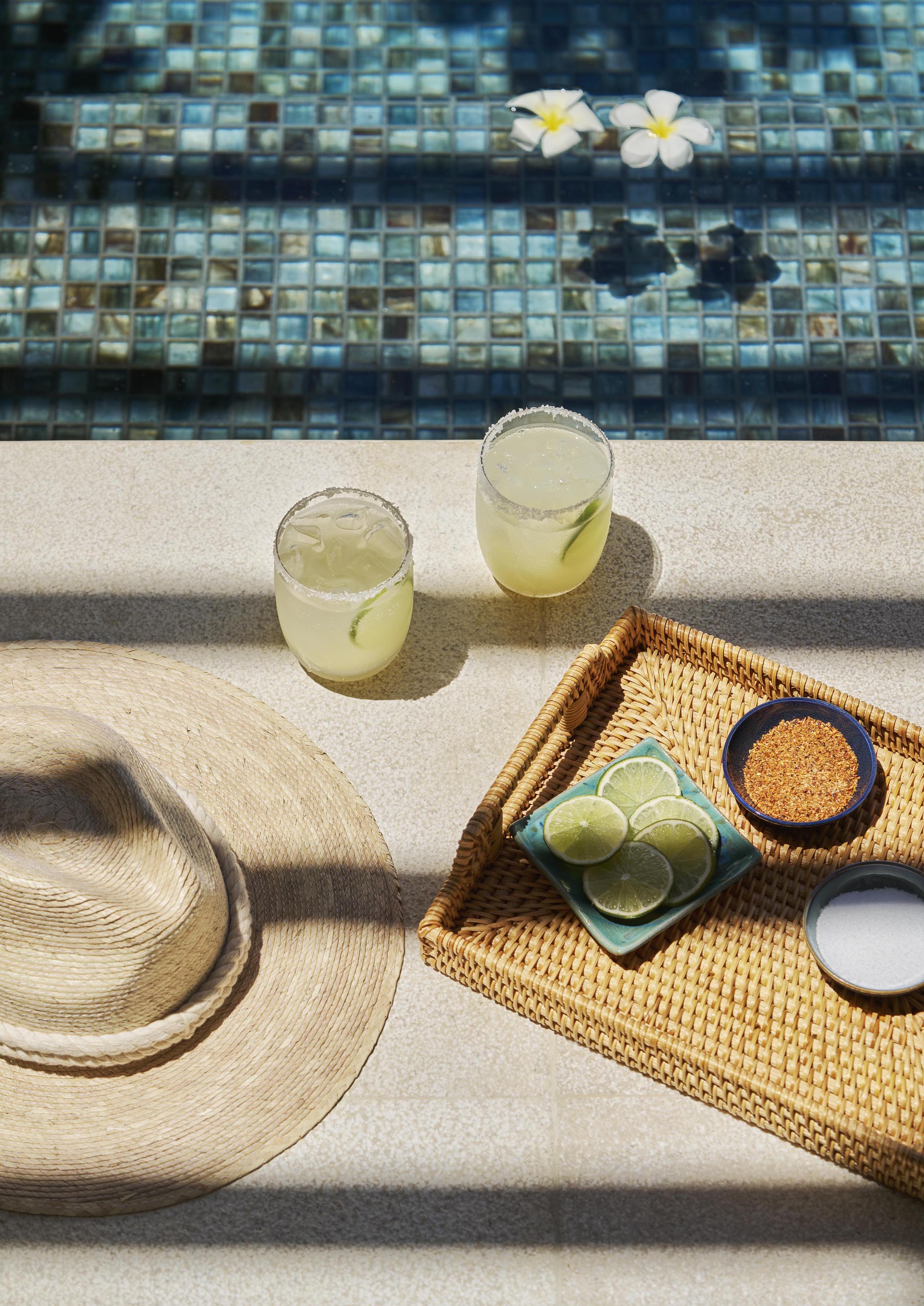 Top down view of resort cadillac margaritas served poolside with salt, lime, and spices on woven tray.