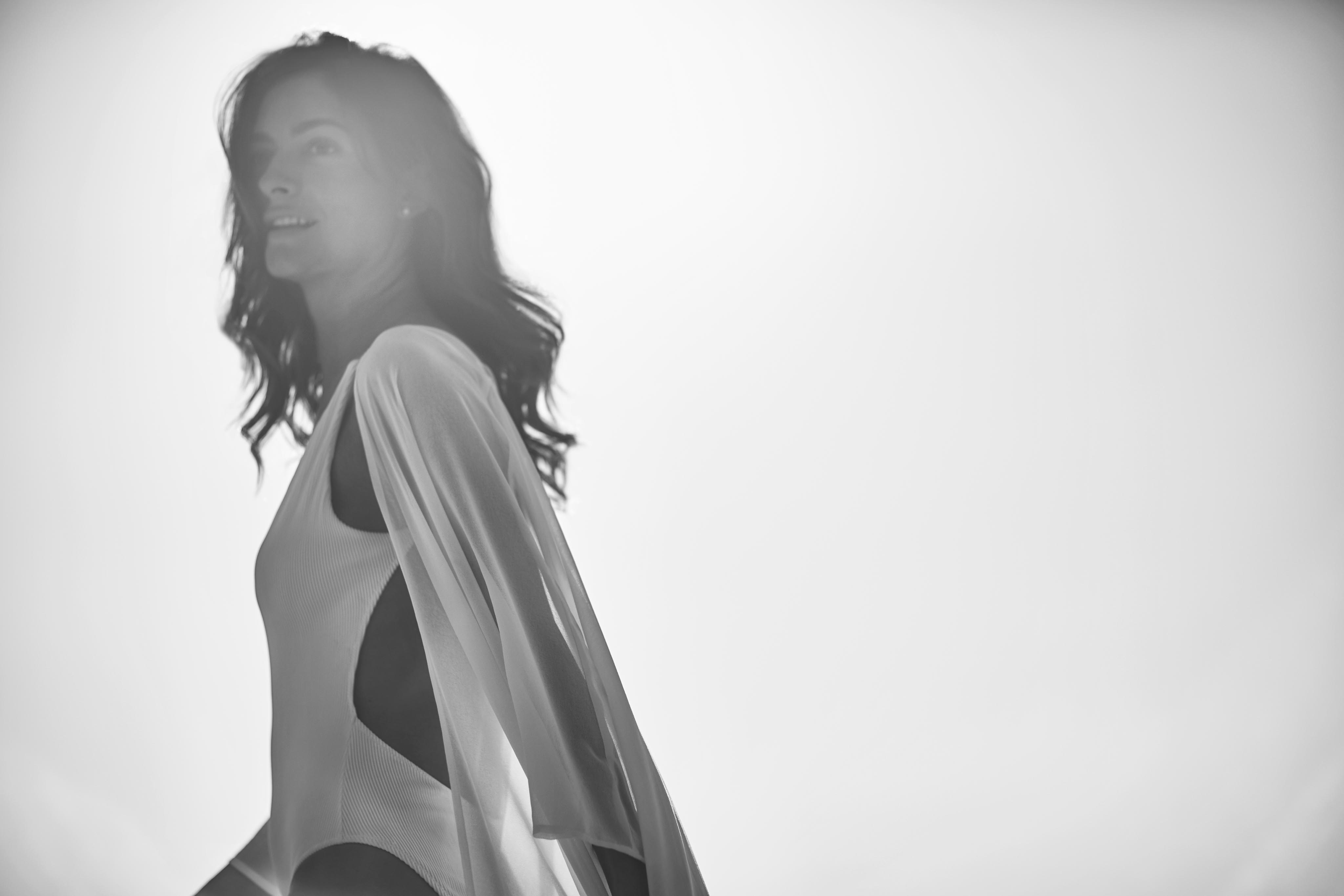 A woman in a flowing outfit is portrayed in side profile against a vibrant, sunlit backdrop, capturing the essence of South America in this black-and-white photograph.