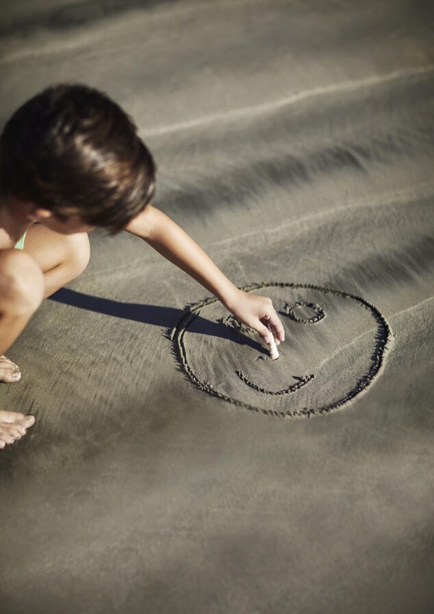 A person crouches on the sandy beaches of Central America, drawing a smiling face with a finger.