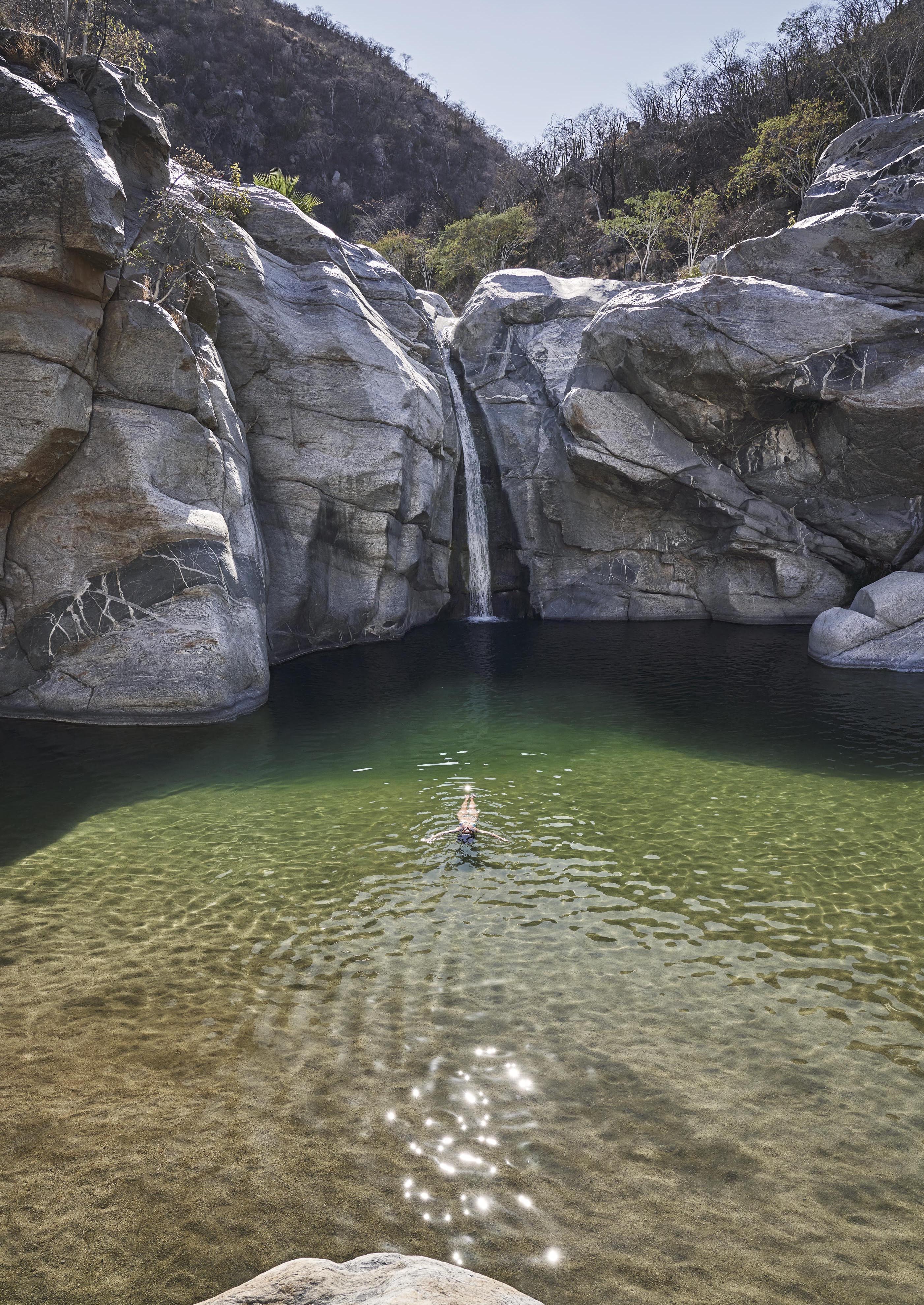 Person floating with arms stretching; private Sol del Mayo small watering hole surrounded by large rock faces and trees