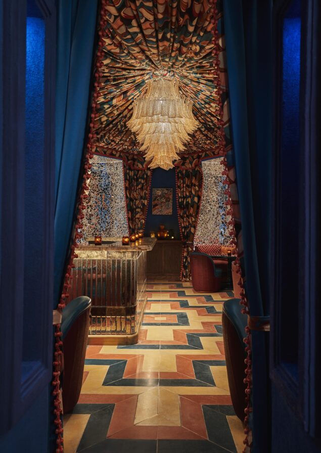 Lavish entrance to dark blue curtain lined entry way of extravagant and artful Los Cabos bar Chiki, designed with colorful custom mosaic tiles and orange, blue, silver, and yellow glass.