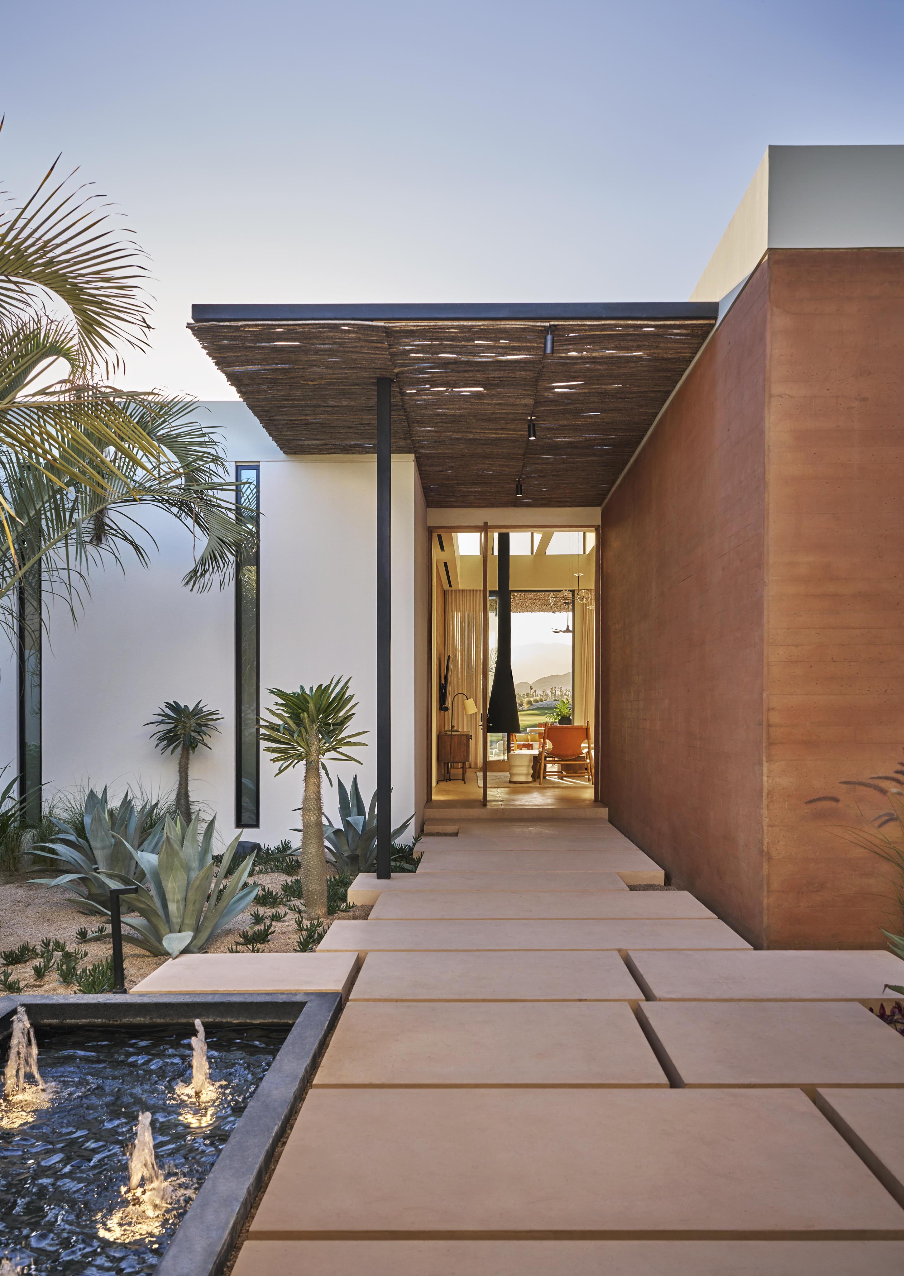 Luxury Four Seasons Los Cabos residences breezeway leading into modern architecture with glimpse of interior as sun peeks into the large glass window in the distance.