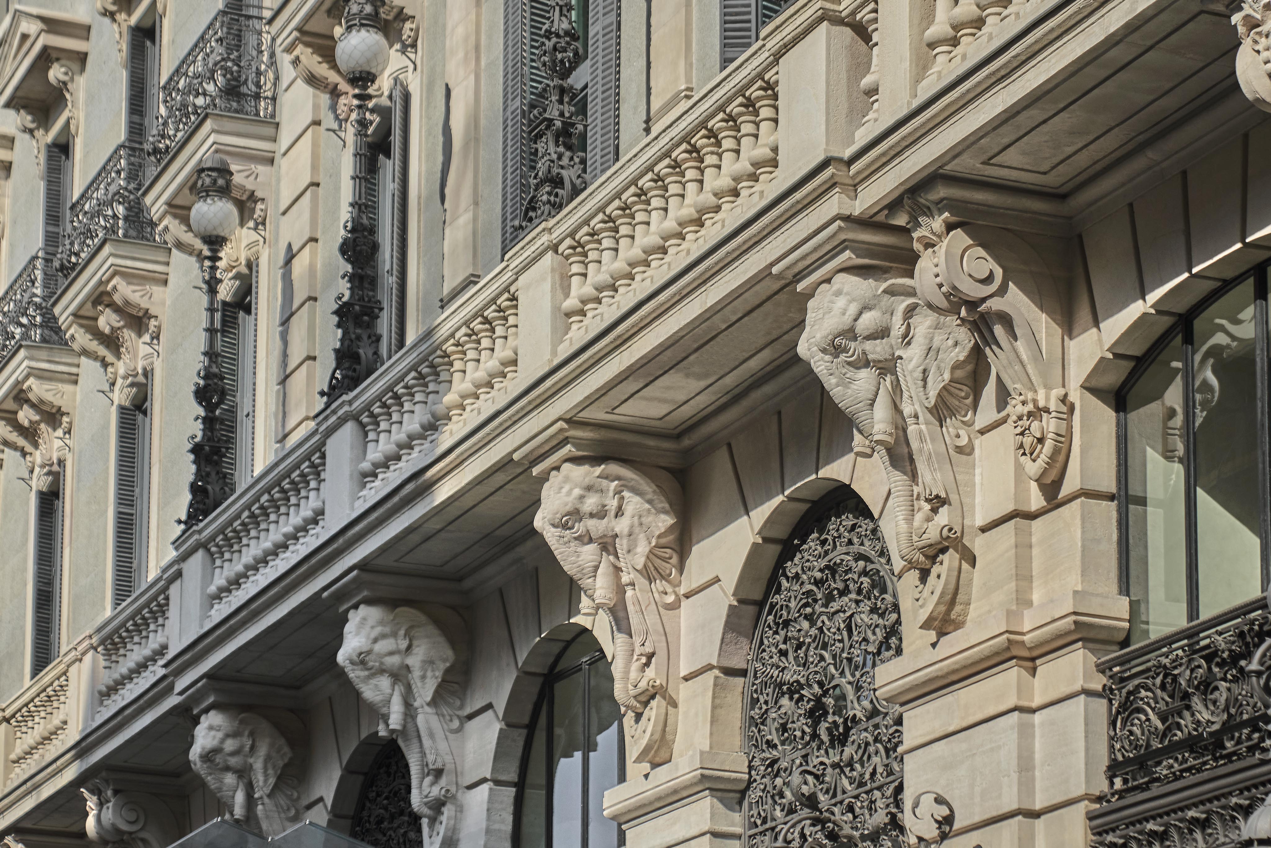 A building facade with ornate architectural details, including sculpted elephant heads and intricate wrought ironwork on the balcony and windows.