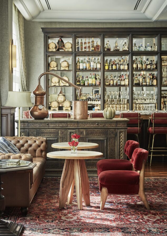 Fifty Mils cafe interior vignette with red velvet chairs, white cafe table, brown leather banquet booth, and luxury bronze accents and sun breaking through the window to the left.
