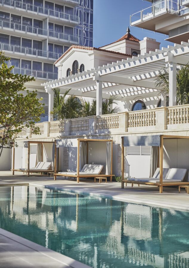 Outdoor Four Seasons Miami Surf Club resort pool with loungers and cabanas, next to a building with Mediterranean architecture and modern upper floors.