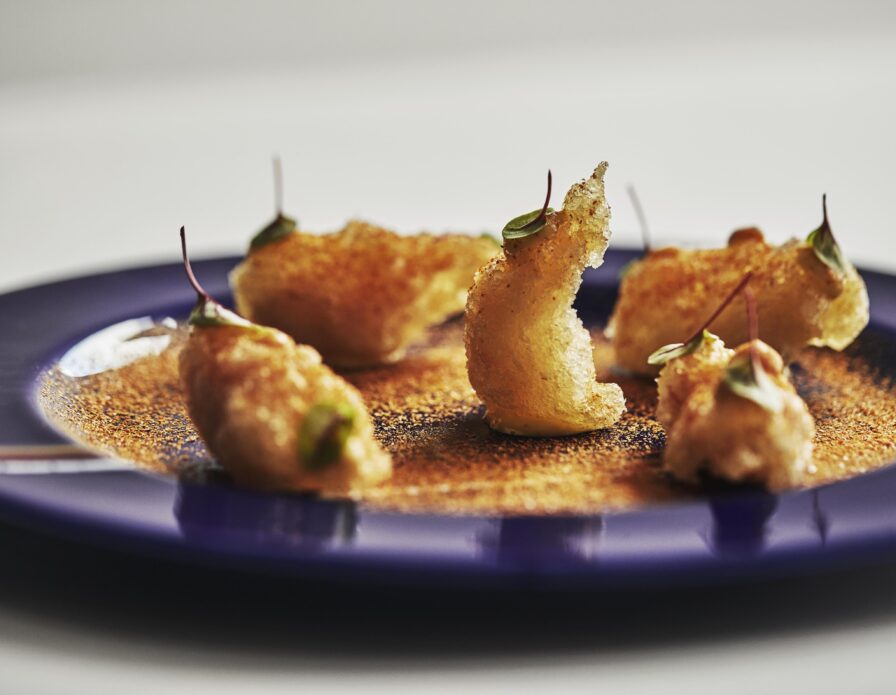 Gourmet dish with artfully arranged fried pieces garnished with microgreens on a blue plate.