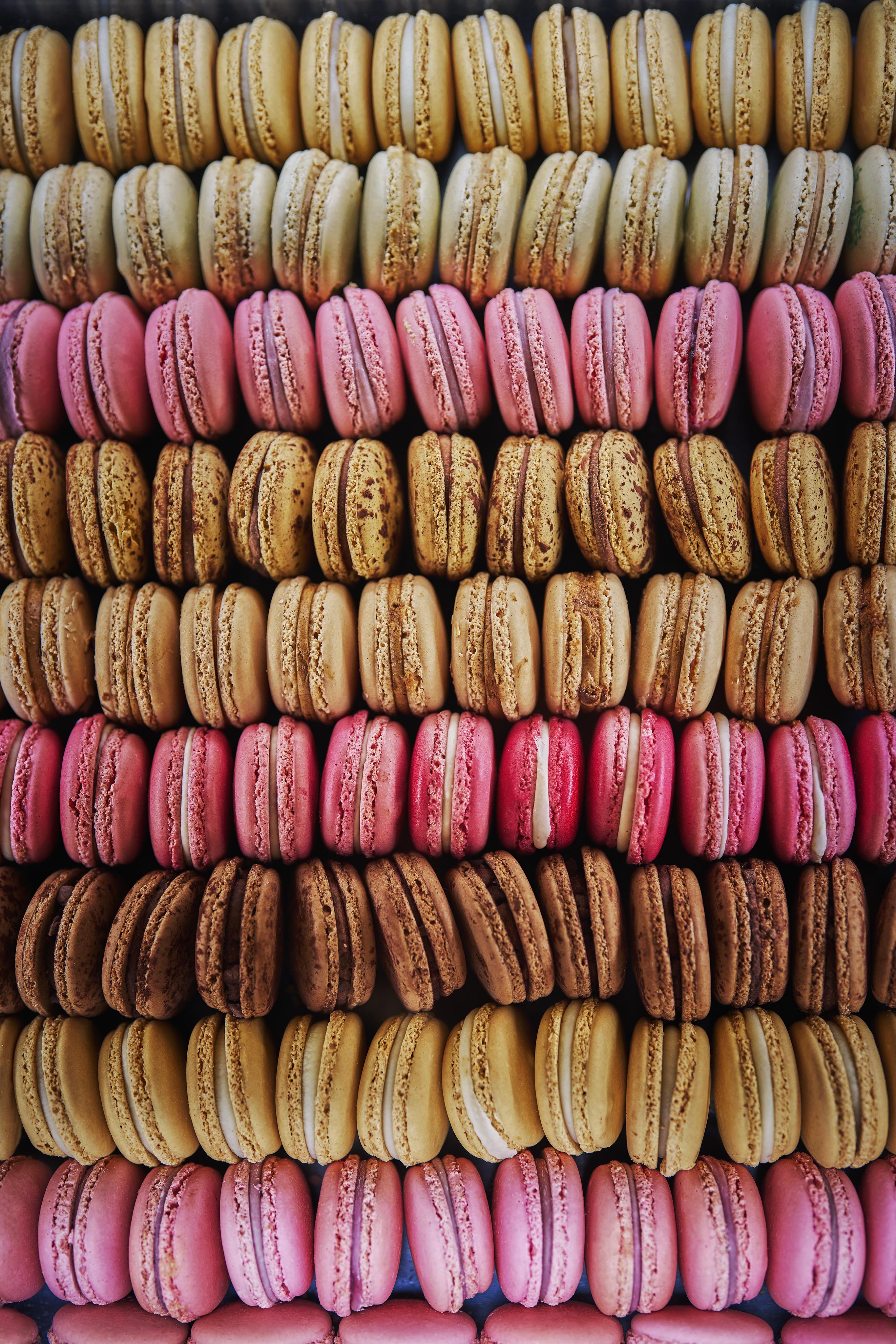 Rows of assorted macarons in pink, yellow, and brown colors are neatly arranged in a close-up view, capturing the elegance often featured in luxury hotel and resort photography across the Middle East.