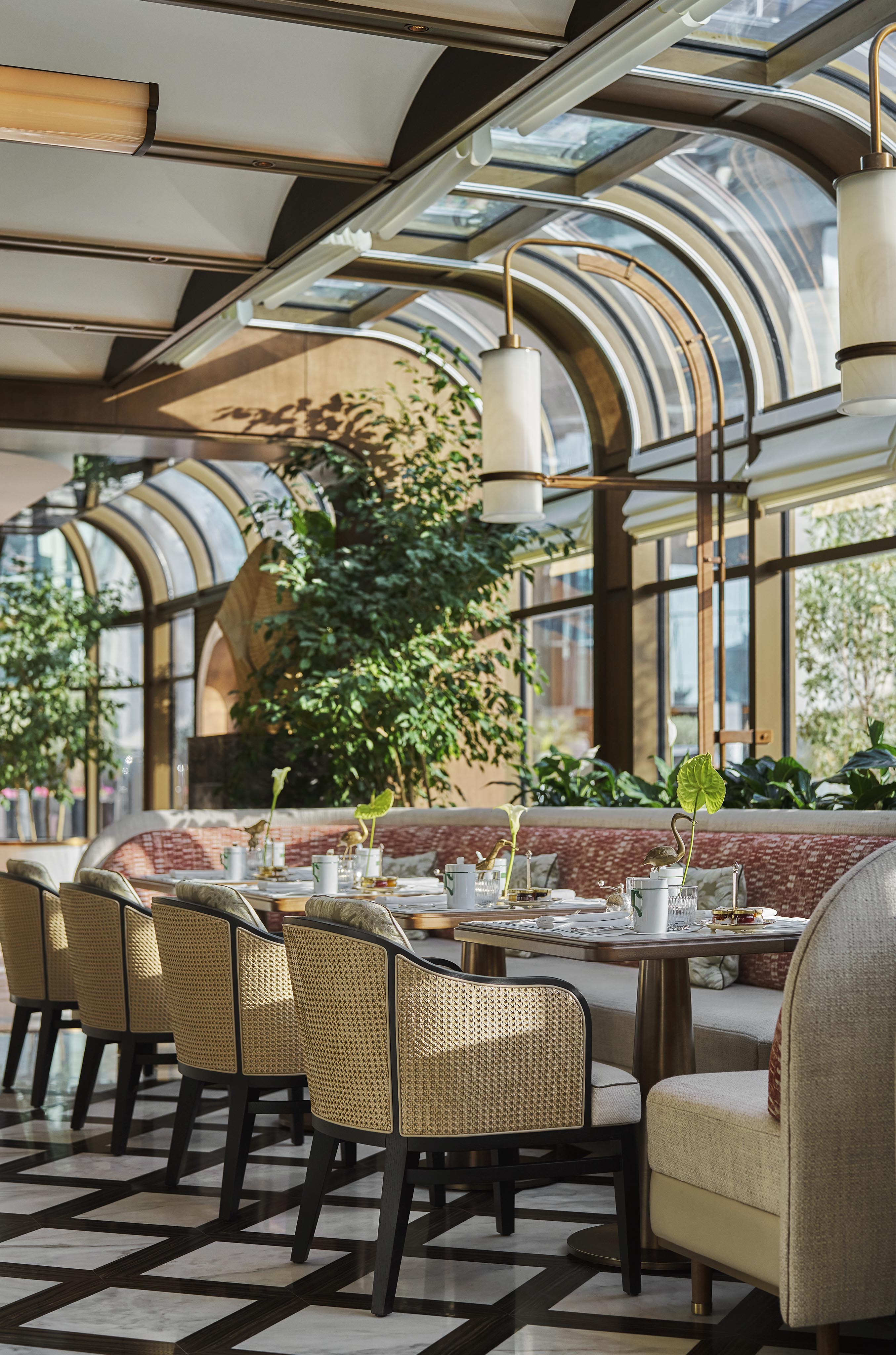 A bright, elegant restaurant interior in a luxury hotel and resort, featuring arched glass windows, cushioned seating, set tables, and potted plants—an inspiring setting for Middle East hospitality photography.