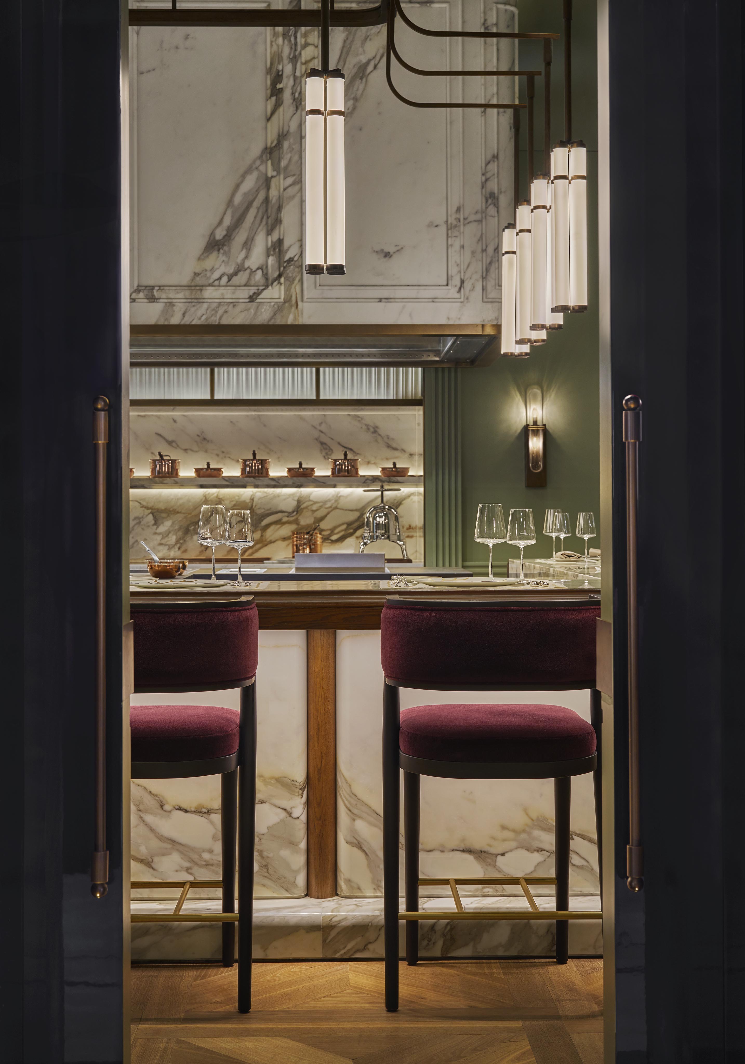 A modern bar with marble surfaces, two burgundy velvet bar stools, hanging pendant lights, and glasses arranged on the counter—perfect for luxury hotel and resort photography in the Middle East.