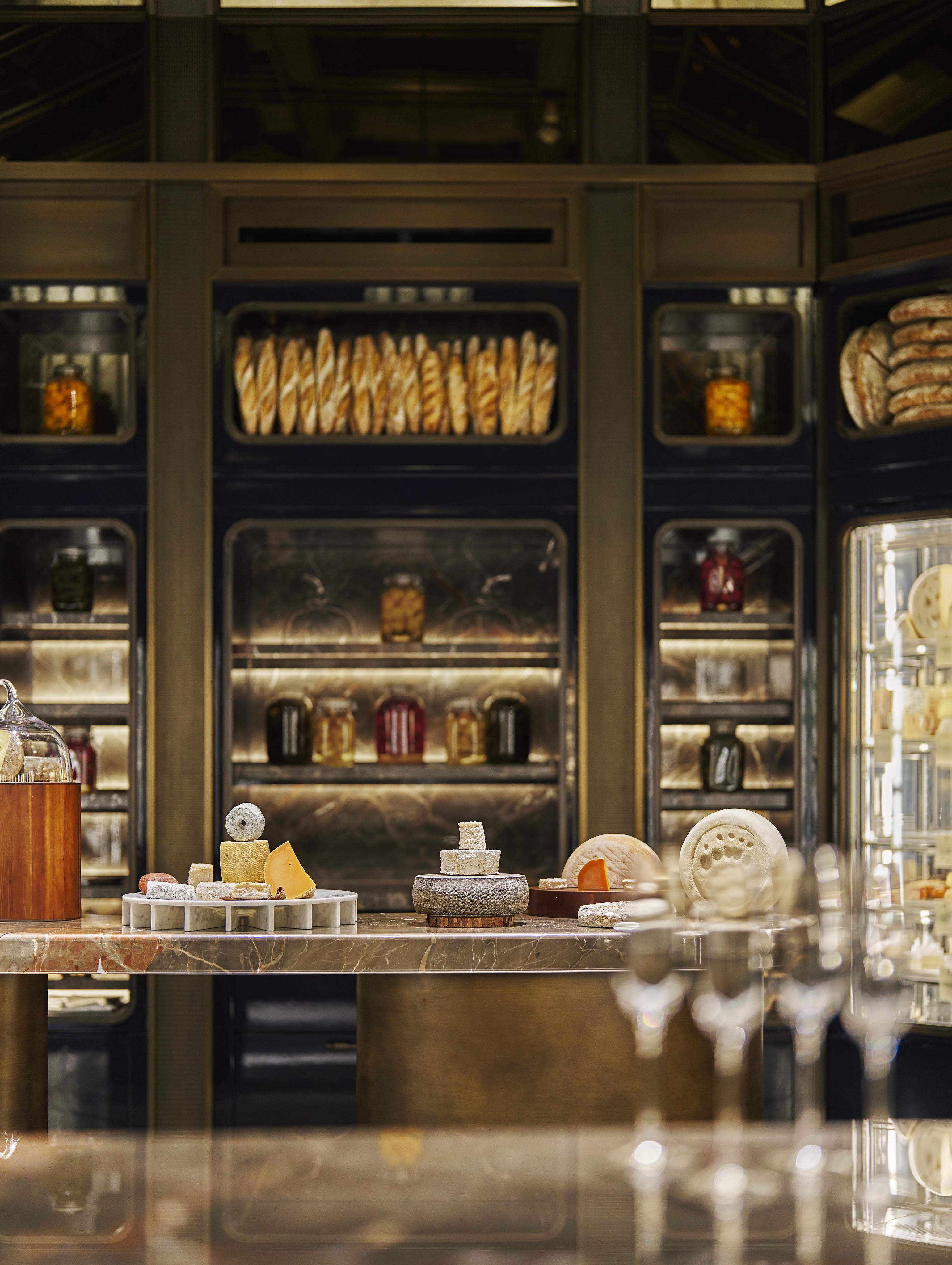 A luxurious kitchen or deli display, captured with the elegance of luxury hotel and resort photography Middle East, featuring assorted cheeses, breads, and jars of preserved foods on sleek shelves and counters.