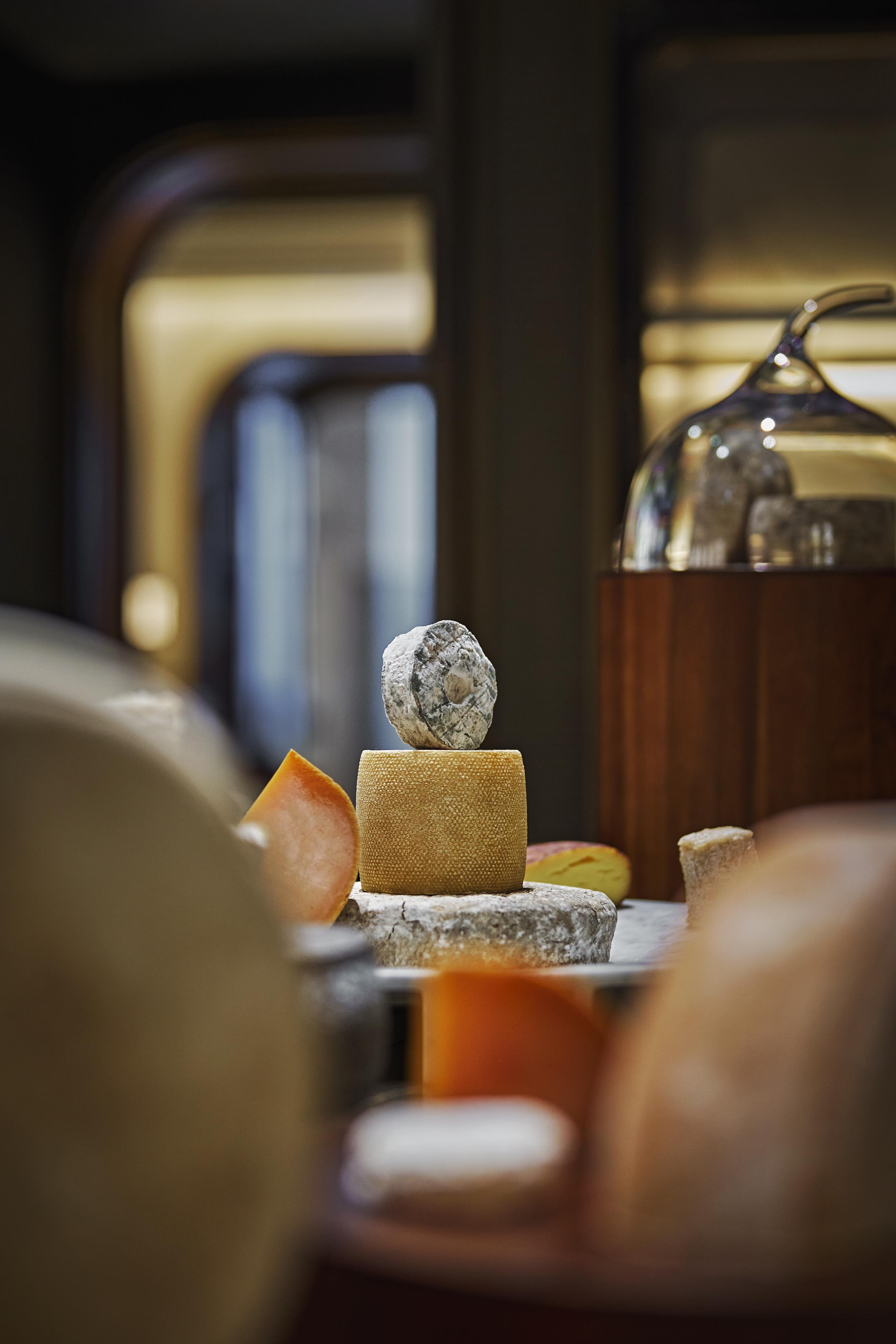A stack of two artisanal cheeses, with a small round cheese atop a larger wheel, displayed on marble among assorted cheeses—evoking the elegance of luxury hotel and resort photography in the Middle East.