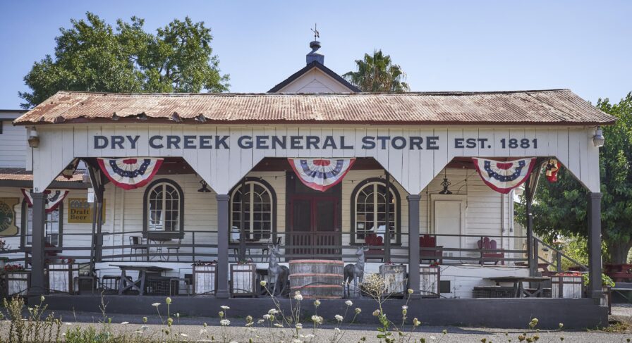 Historic Dry Creek General Store, established in 1881, with a rustic facade and decorative flags, surrounded by trees.