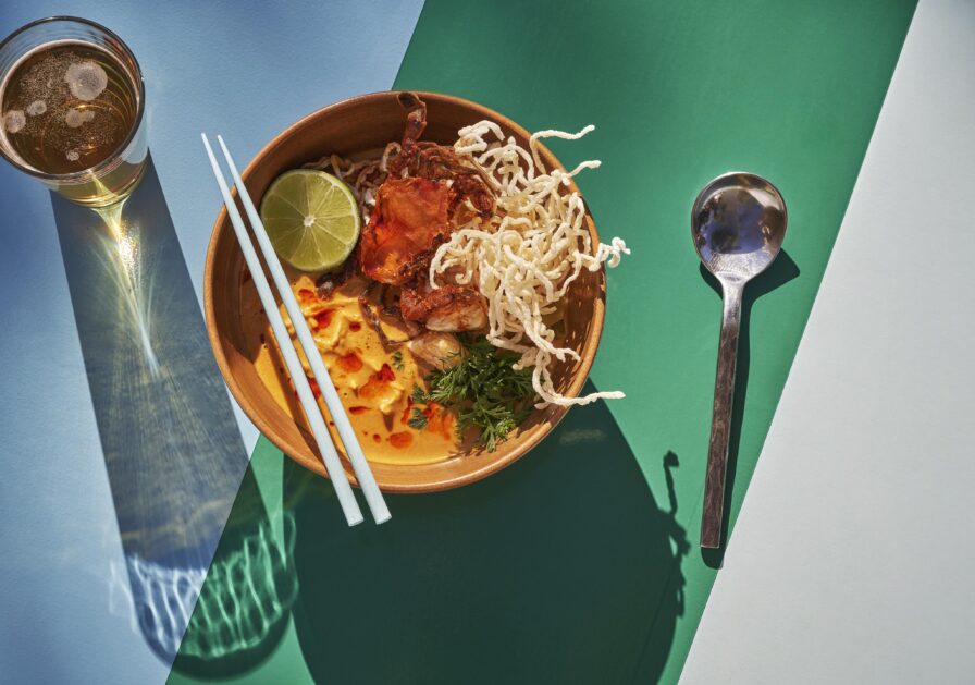 Aerial view of bright colored ramen dish served on white and green tabletop with long shadows from Montage Los Cabos resort restaurant; Talay