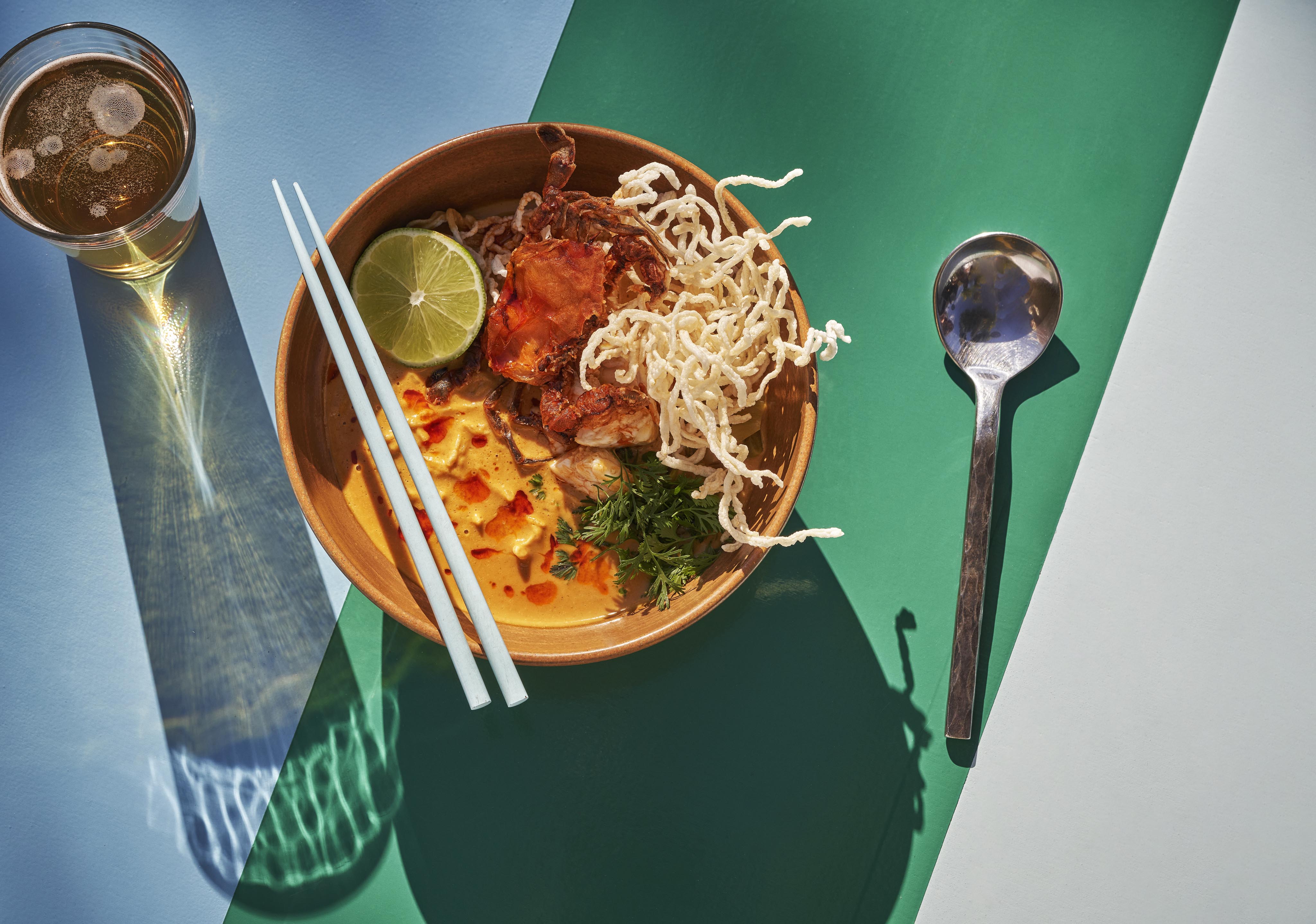 Aerial view of bright colored ramen dish served on white and green tabletop with long shadows from Montage Los Cabos resort restaurant; Talay