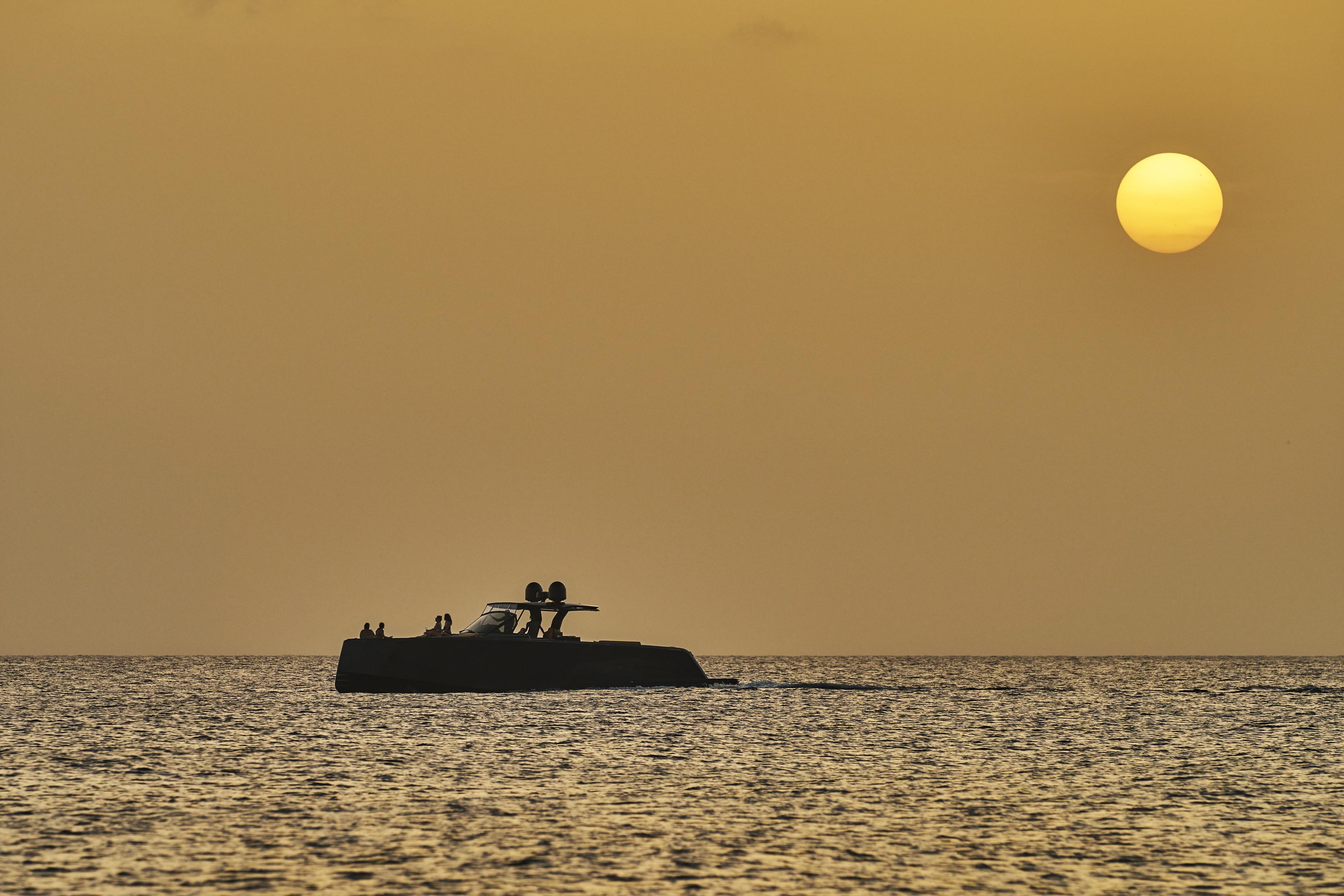 A boat on a calm sea during sunset, with a clear sky and the sun near the horizon.
