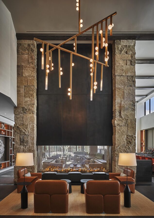 A modern Pendry Park City interior lounge area inspired by the Rockies, featuring warm leather furnishing, fireplace and a large geometric chandelier hanging overhead.