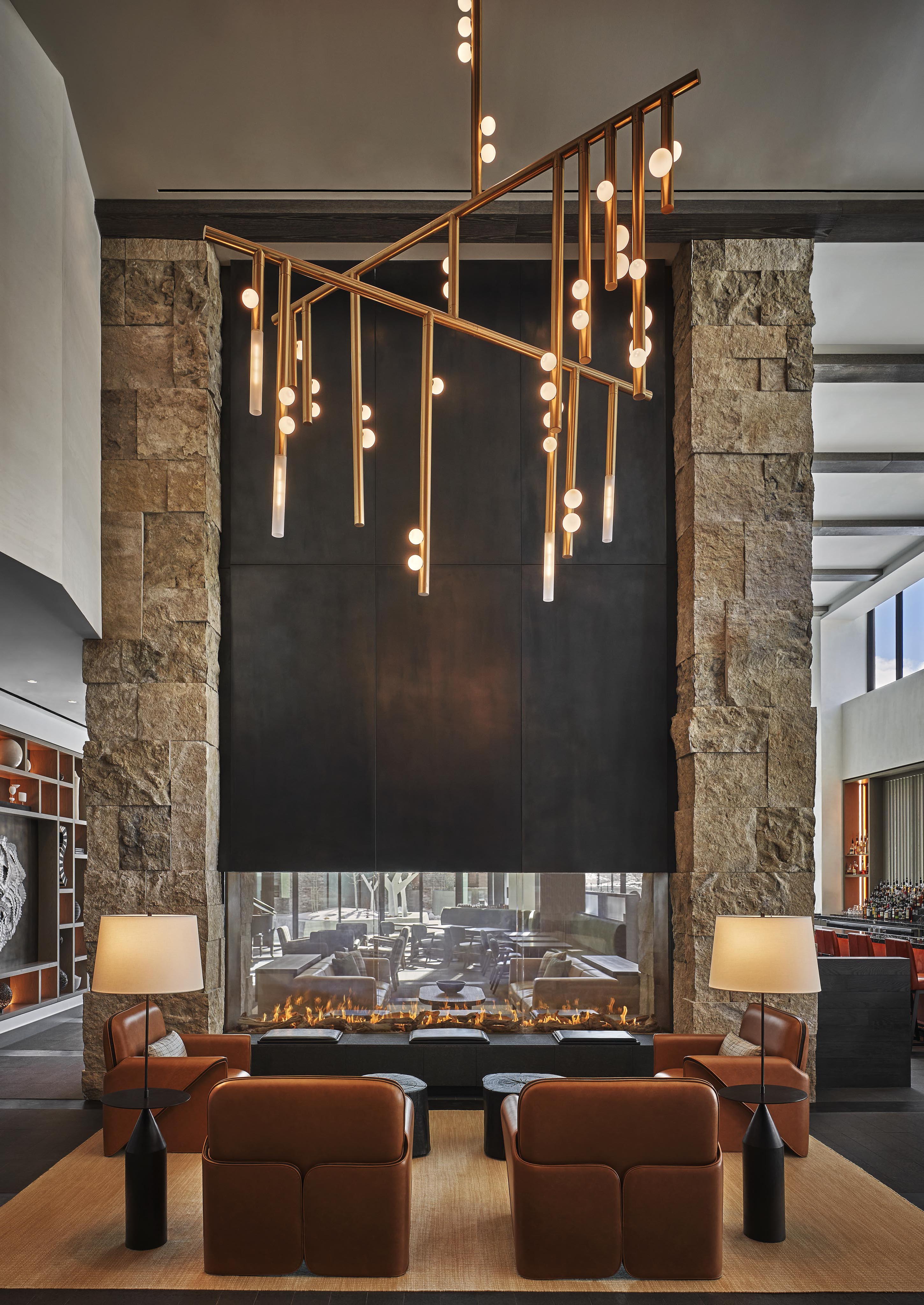 A modern Pendry Park City interior lounge area inspired by the Rockies, featuring warm leather furnishing, fireplace and a large geometric chandelier hanging overhead.