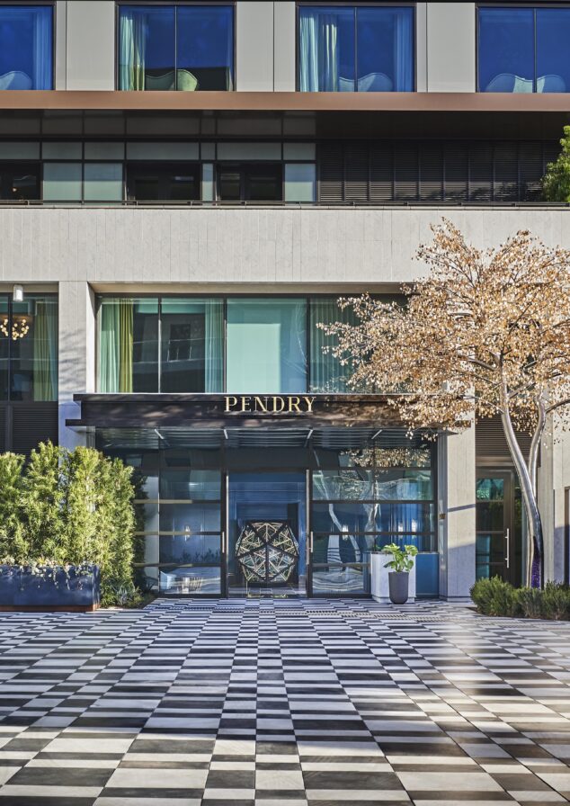 Modern Pendry West Hollywood hotel entrance with large glass doors, a canopy labeled "Pendry," and a geometric-patterned checkered patio. The building has reflective windows and minimalistic landscaping.