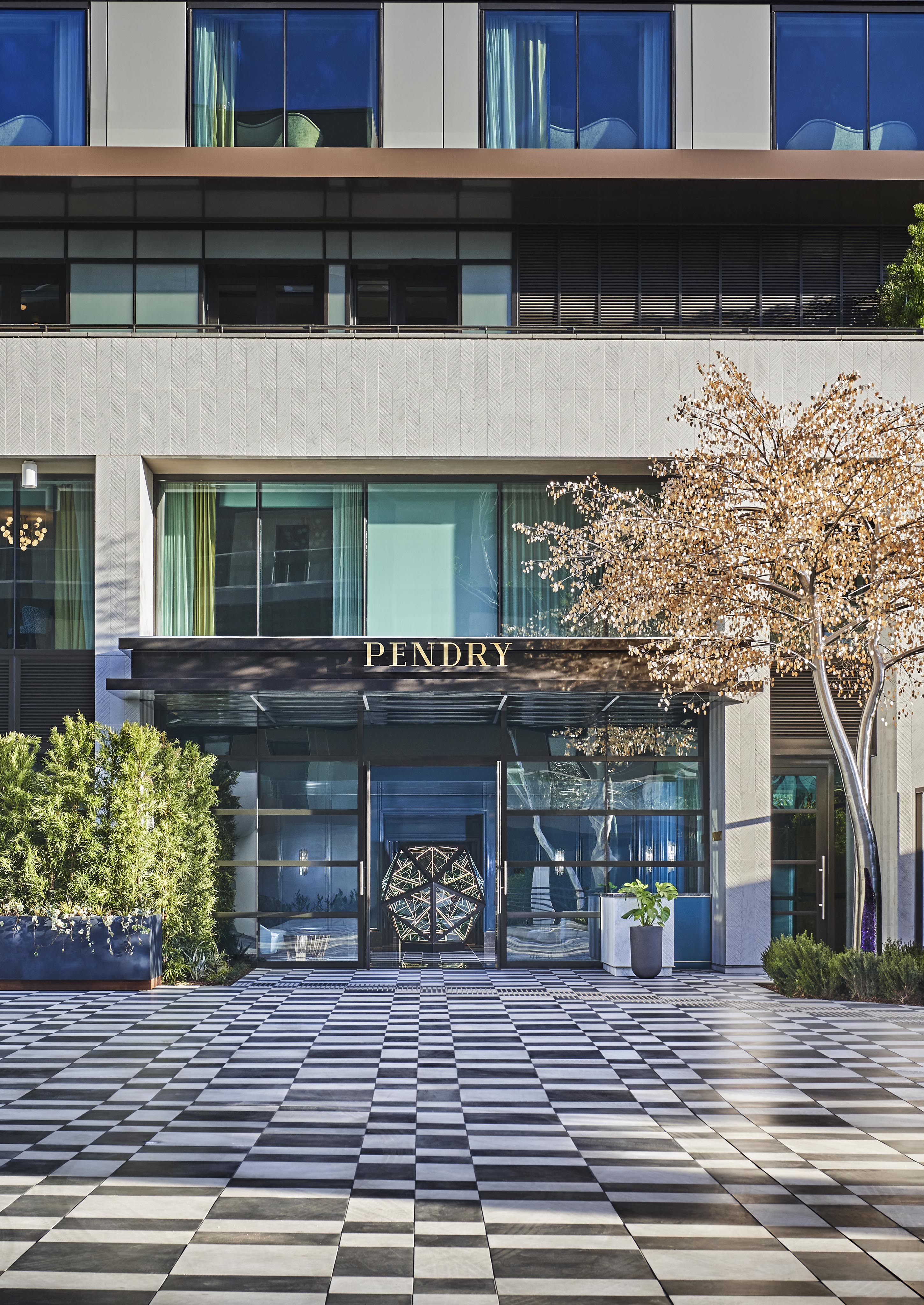 Modern Pendry West Hollywood hotel entrance with large glass doors, a canopy labeled "Pendry," and a geometric-patterned checkered patio. The building has reflective windows and minimalistic landscaping.